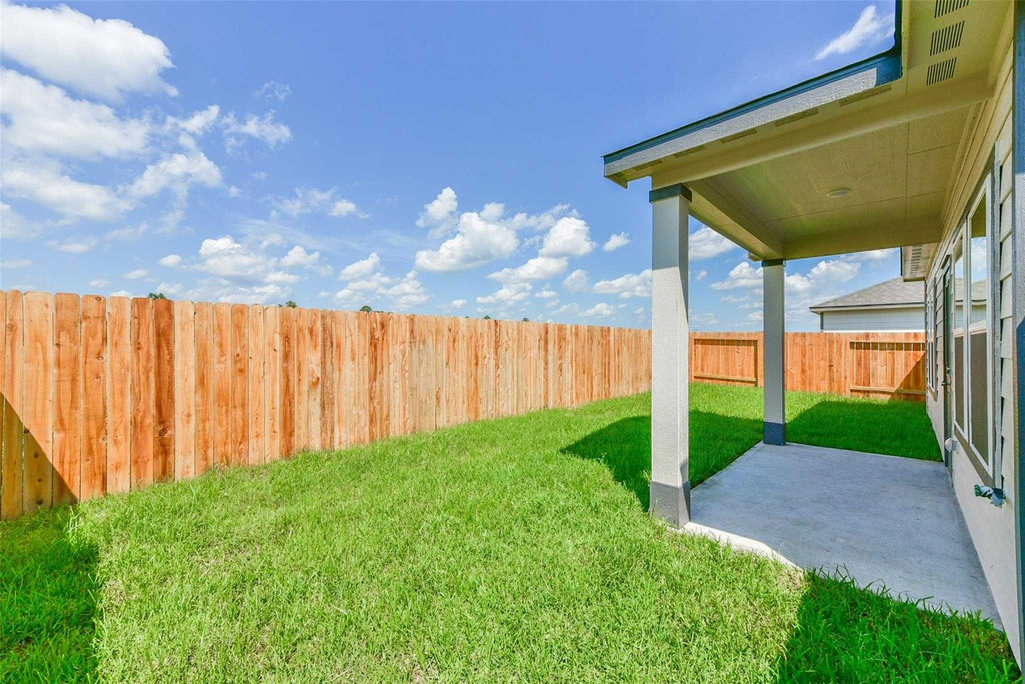 Covered back patio with wooden fence and lush green yard in Davidson Homes The Sabine E, The Villages at WestPointe, Dayton, Texas