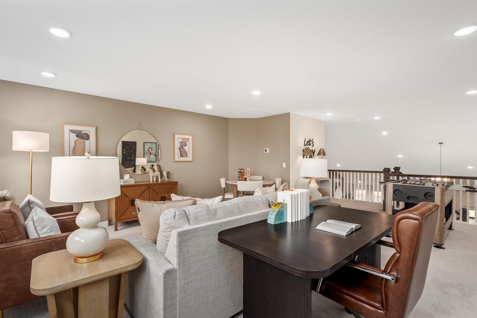 Cozy upstairs loft in The Ridgeport home: beige sectional sofa, wooden desk, leather chair, abstract art, lamps, and staircase railing