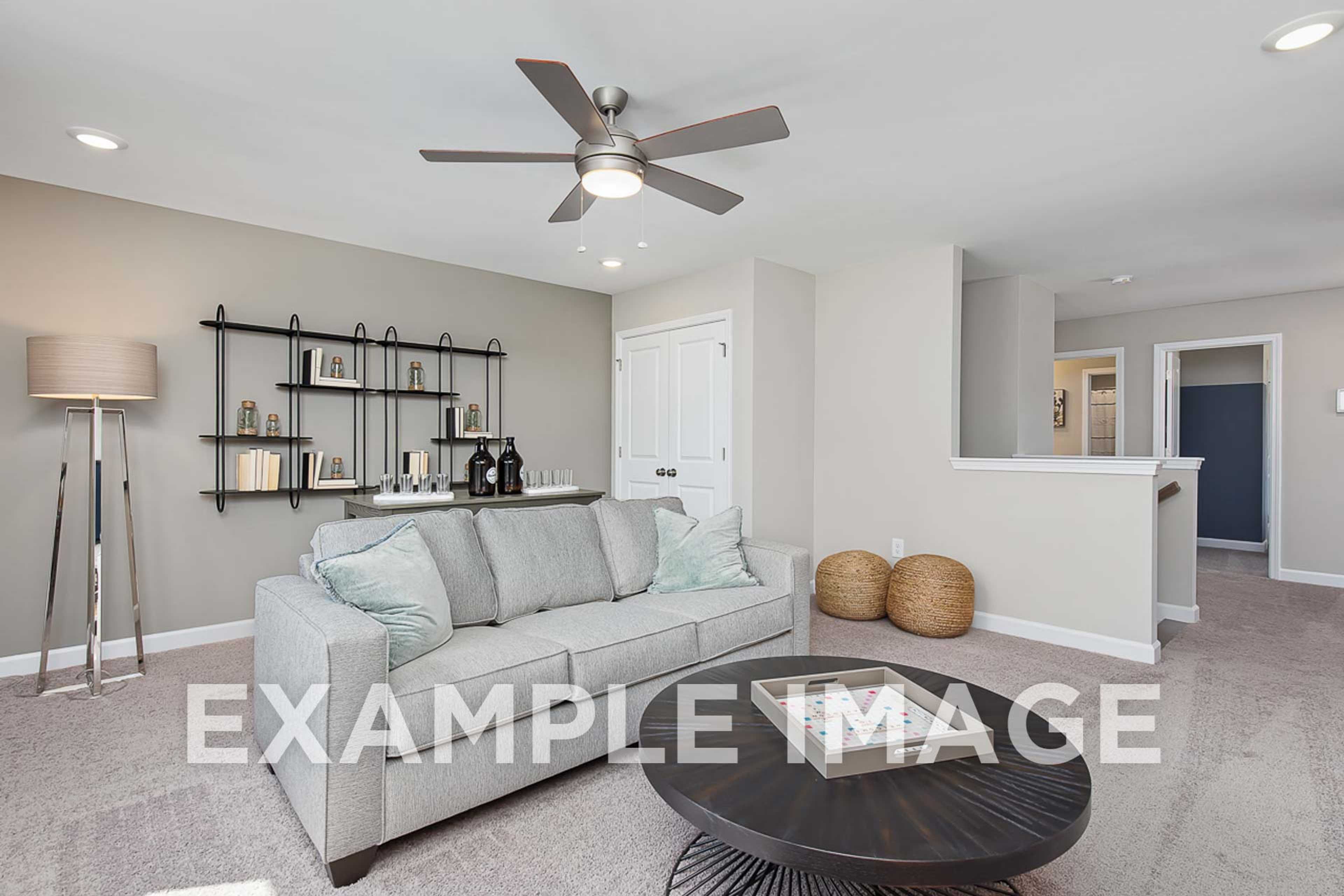 Spacious living room in The Ash D by Davidson Homes with gray sofa, ceiling fan, built-in shelves, and open upper floor layout