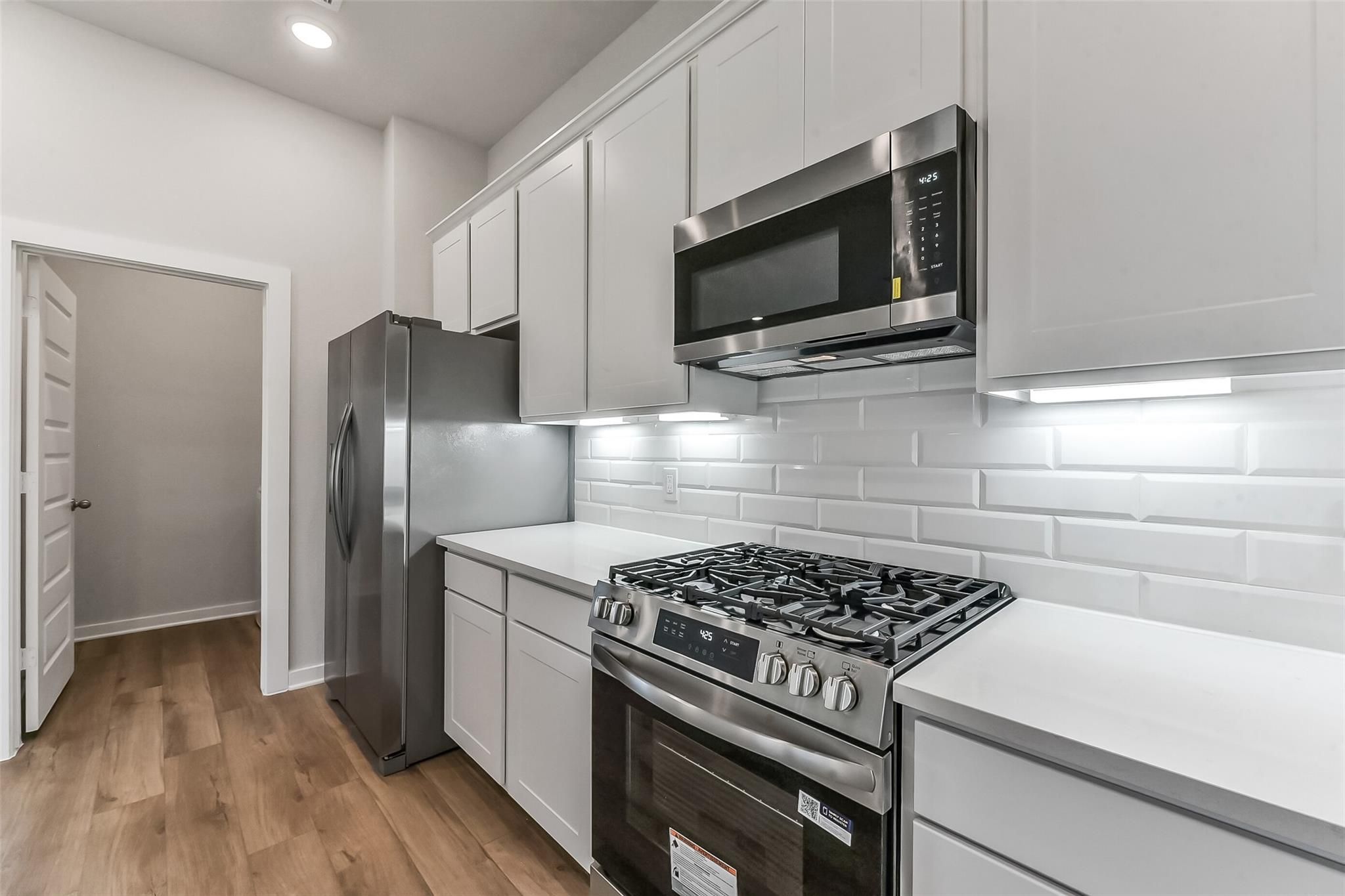 Modern white shaker kitchen with stainless gas range, fridge, microwave, subway tile backsplash in Davidson Homes The Costa B, Dayton, TX