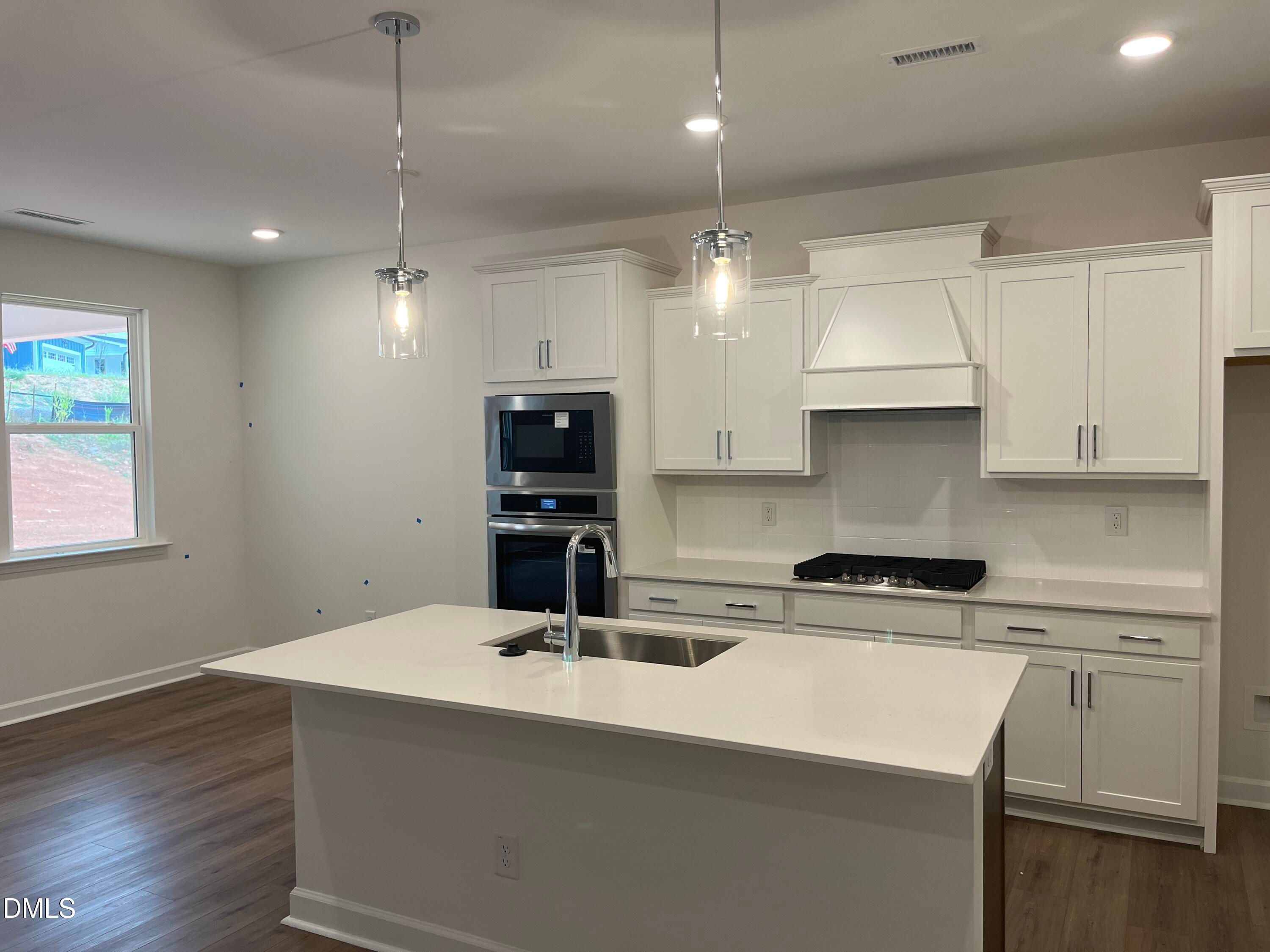 Kitchen island with white cabinetry, gas cooktop, and stainless appliances in Davidson Homes The Willow G, Wake Forest, NC