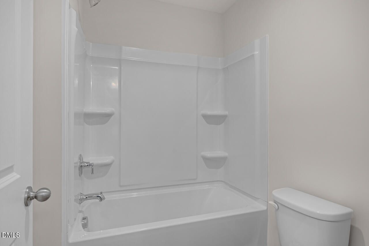 Clean white bathtub-shower combo with glass enclosure and shelves in guest bath of Davidson Homes The Cypress D II, Angier, NC