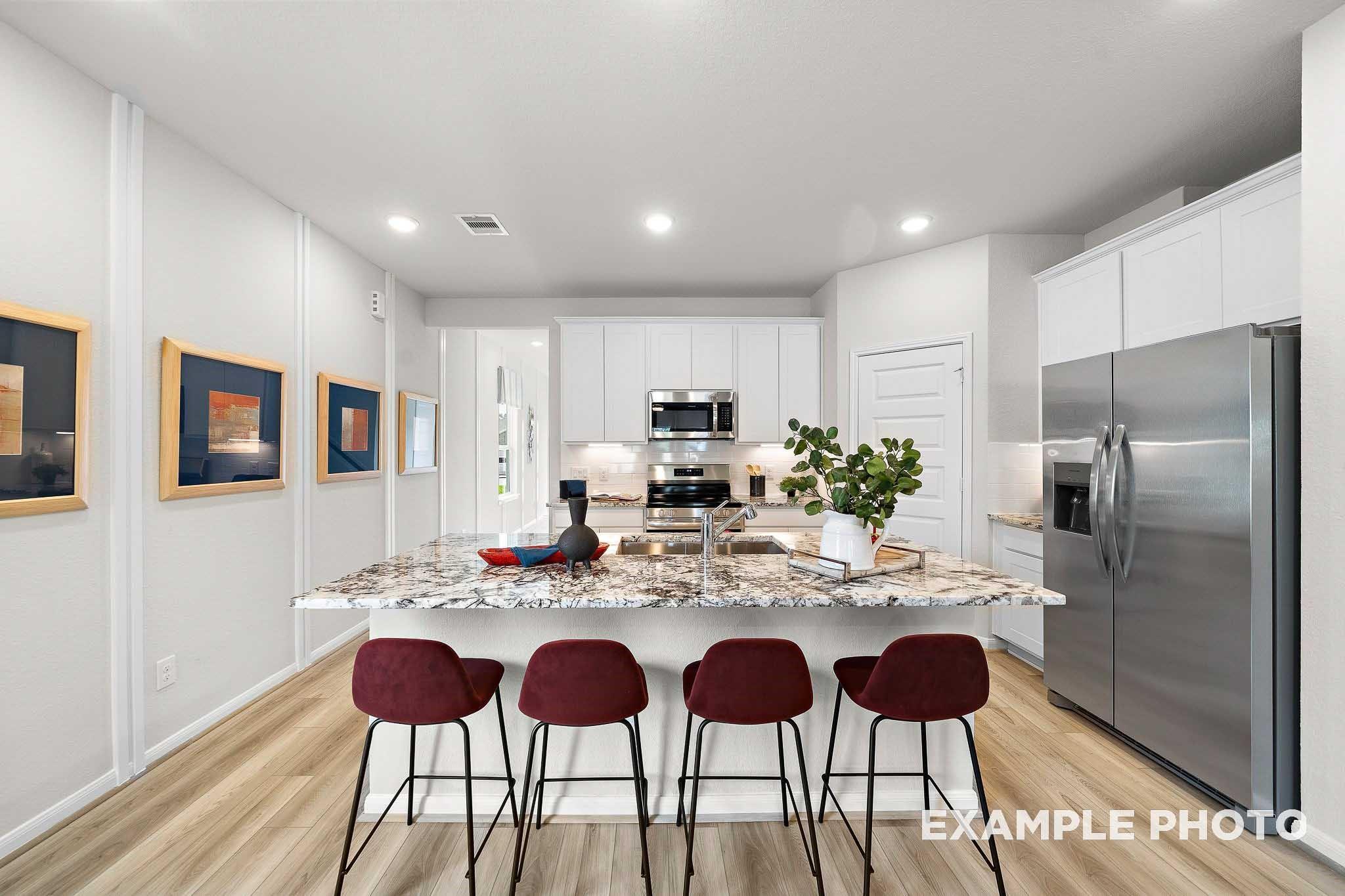 Modern kitchen with white cabinets, granite island, stainless appliances, and red bar stools in 5-bedroom San Marcos E home, Conroe, Texas