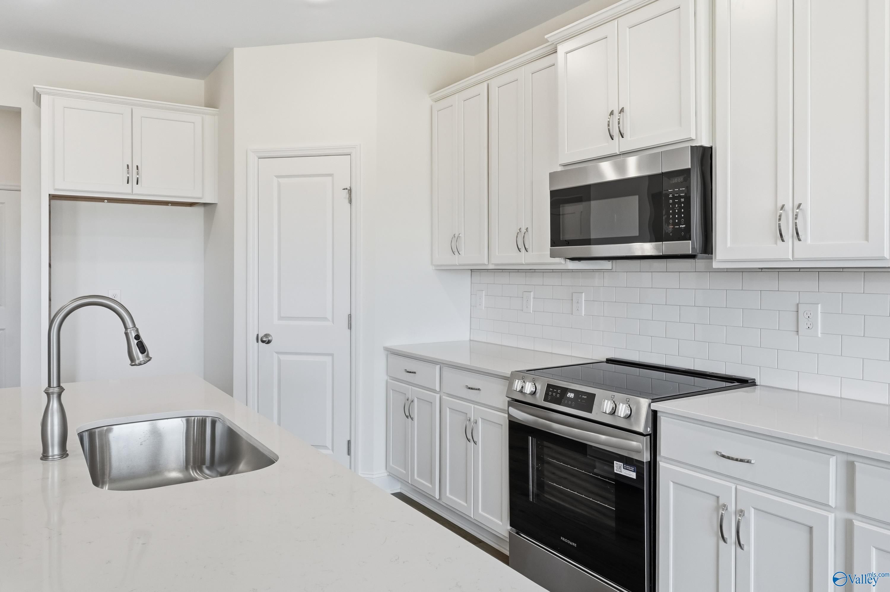Modern white kitchen with stainless steel appliances, subway tile backsplash, and quartz island in Davidson Homes Montgomery C, Harvest, AL