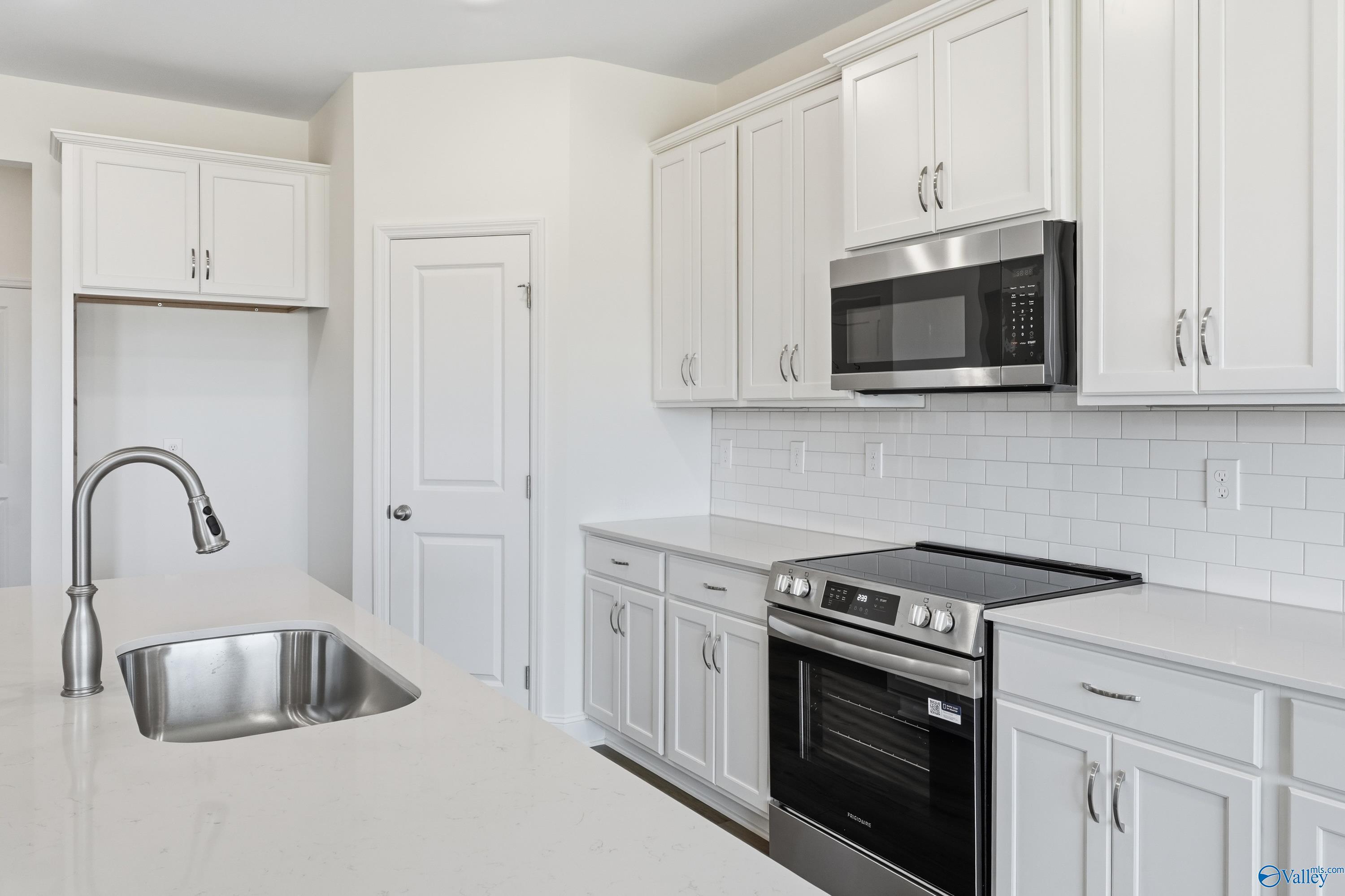 Modern white kitchen with stainless steel appliances, subway tile backsplash, and quartz island in Davidson Homes Montgomery C, Harvest, AL