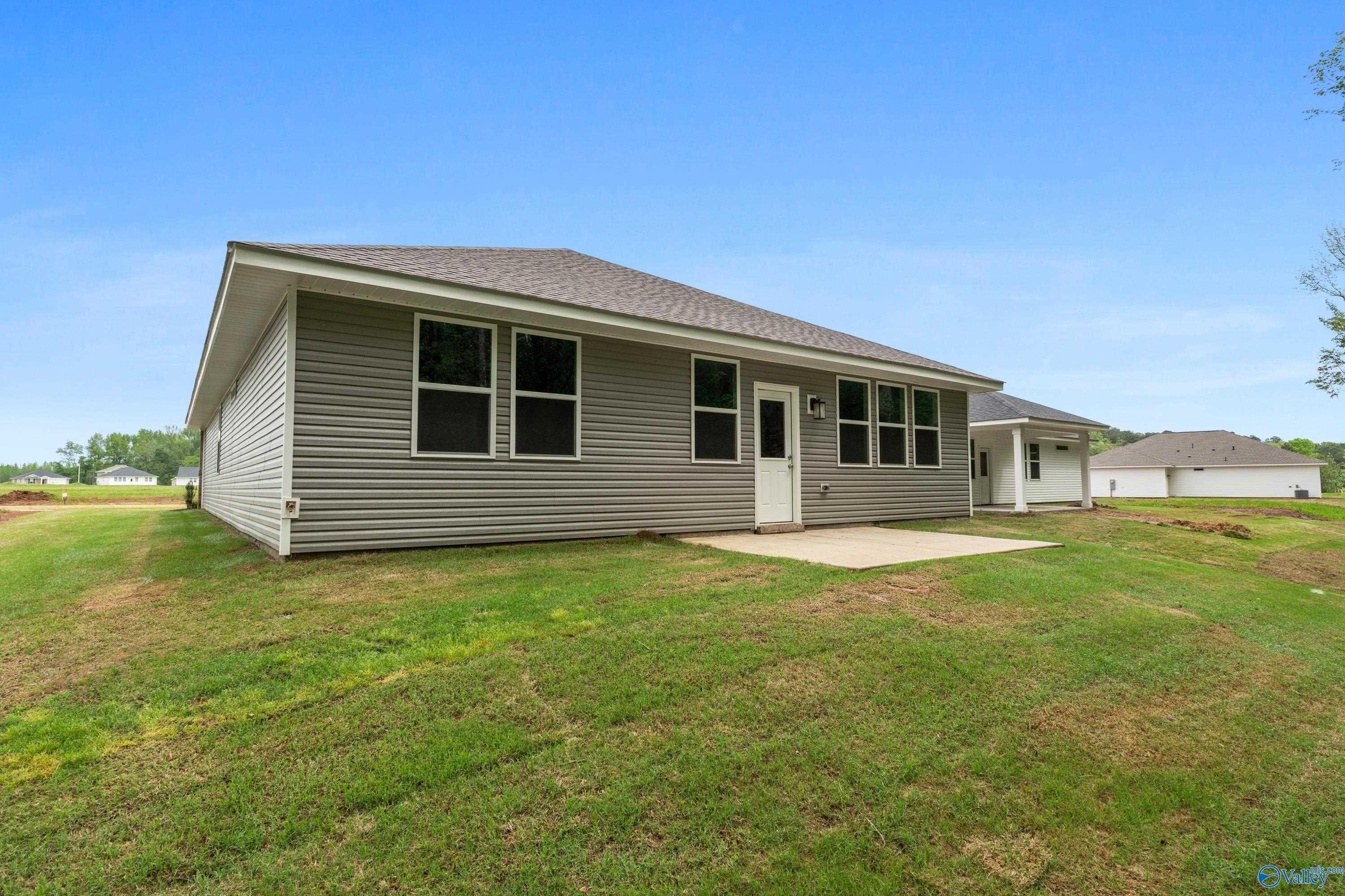 Side view of gray-sided single-story The Luna home by Davidson Homes with covered porch, lush green backyard in Forest Glen, Hazel Green, Alabama