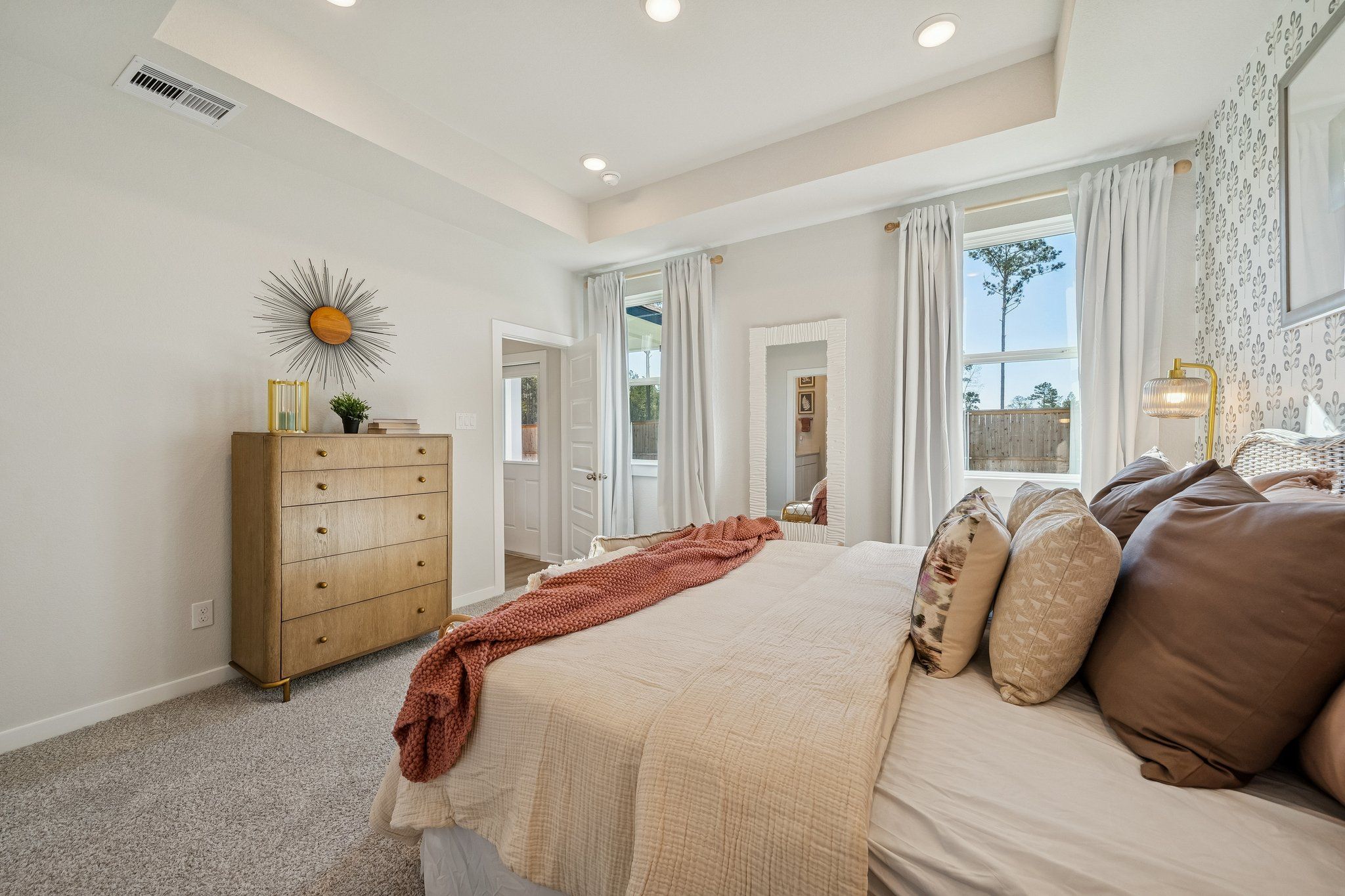 Elegant master bedroom at Spring Branch Crossing in Conroe Texas with plush neutral bed wood dresser sheer curtains
