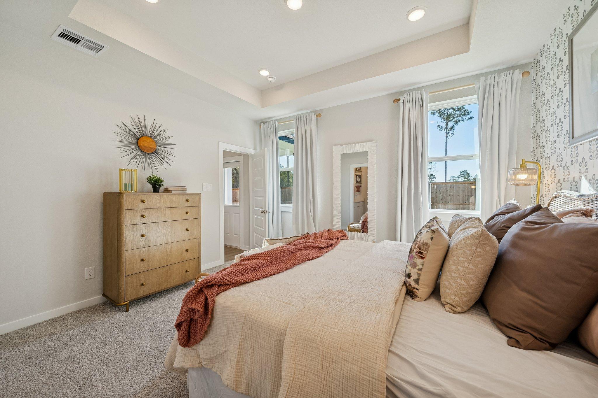 Elegant master bedroom at Spring Branch Crossing in Conroe Texas with plush neutral bed wood dresser sheer curtains