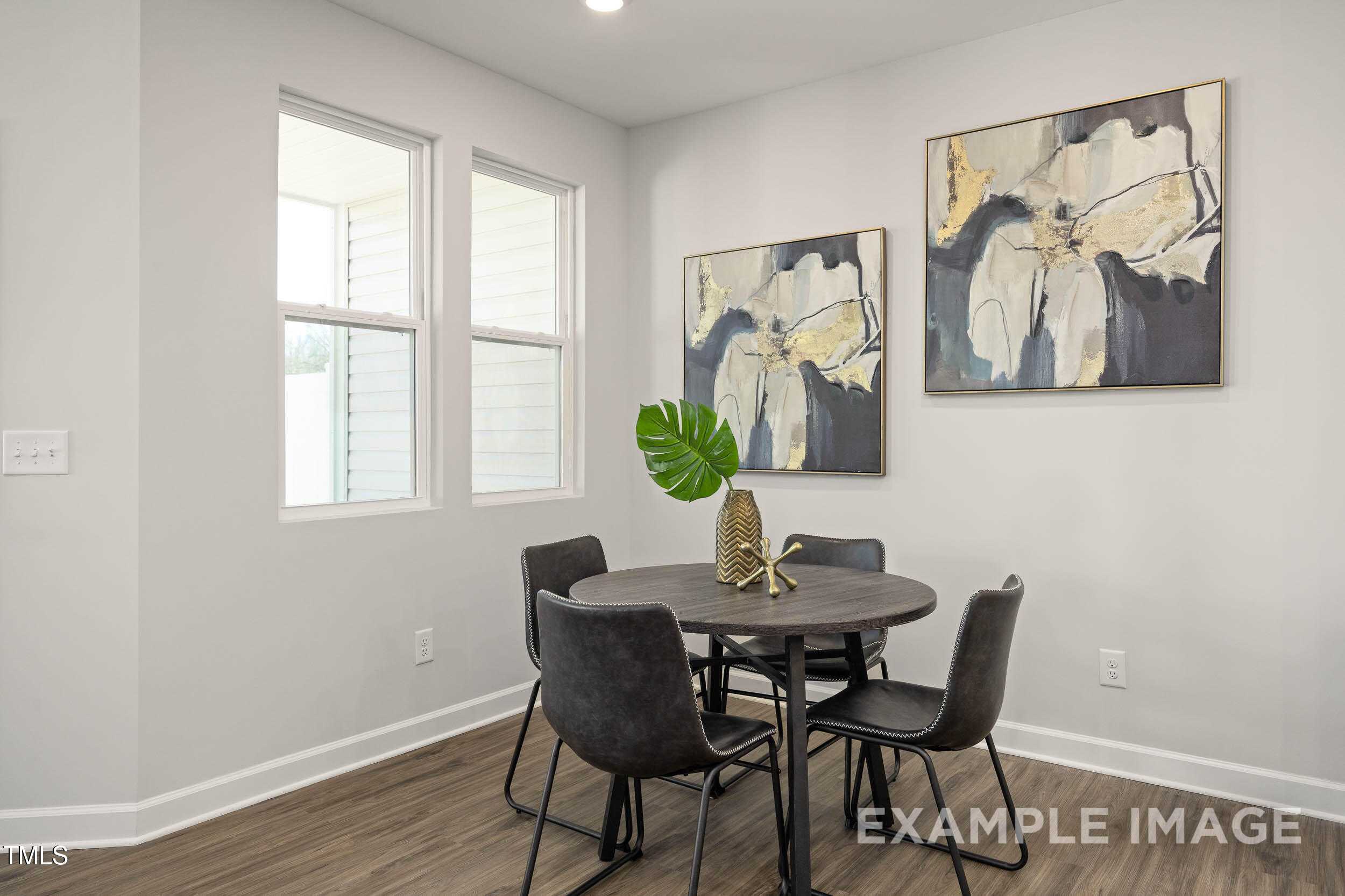 Modern dining nook with round wood table, leather chairs, monstera plant, and abstract gold art in The Graham Interior by Davidson Homes, Fuquay-Varina, NC