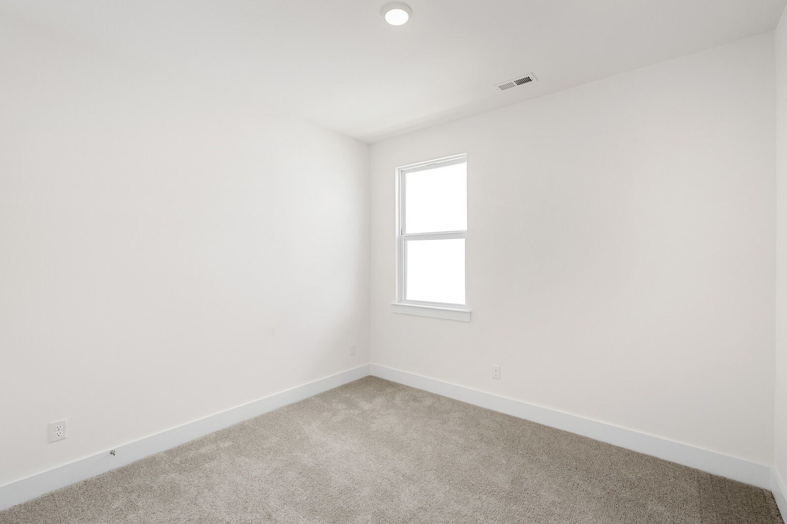 Bright, carpeted bedroom in The Cottonwood home design by Davidson Homes with neutral walls and a single window.