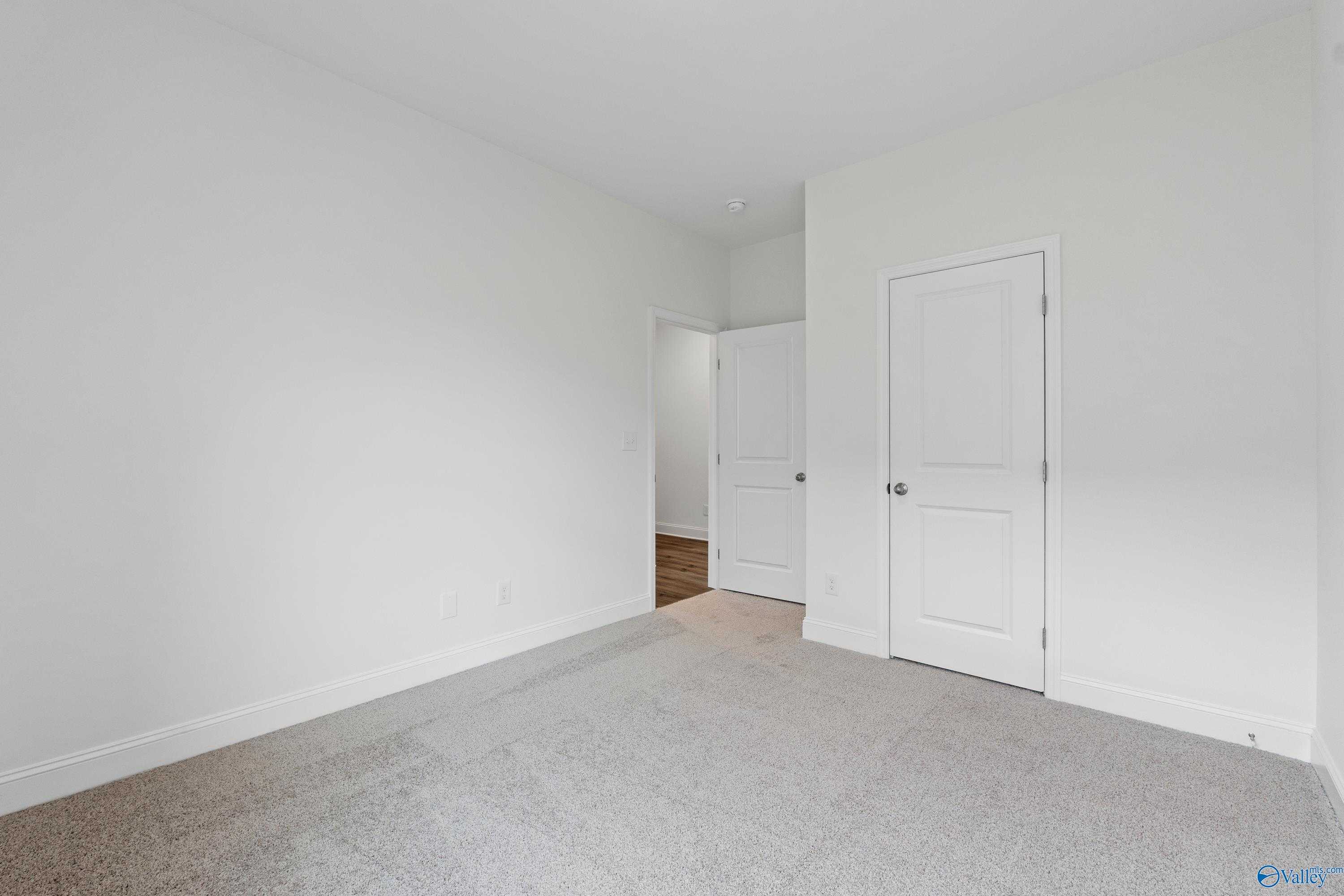 Bright secondary bedroom with white walls, gray carpet, open doorway, and closet door in Davidson Homes The Asheville C, Athens AL
