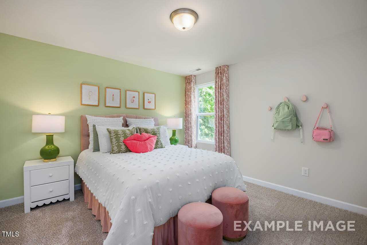 Cozy girl's bedroom with green walls, pink pillows on polka-dot bed, green lamps, floral window in Davidson Homes The Willow G, Angier, NC
