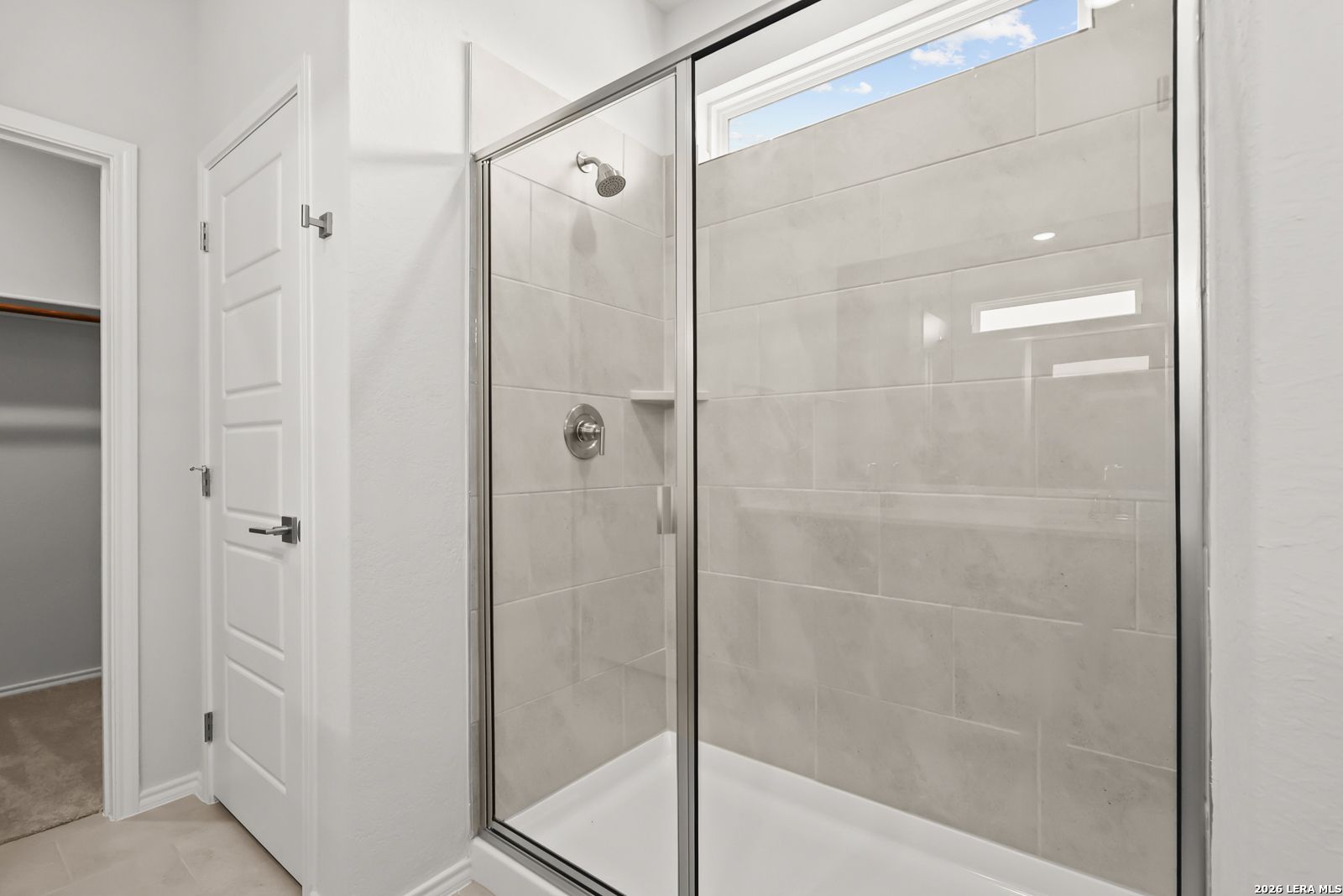 Glass-enclosed tile shower with transom window in master bathroom of Davidson Homes The Daphne I in Bricewood, San Antonio