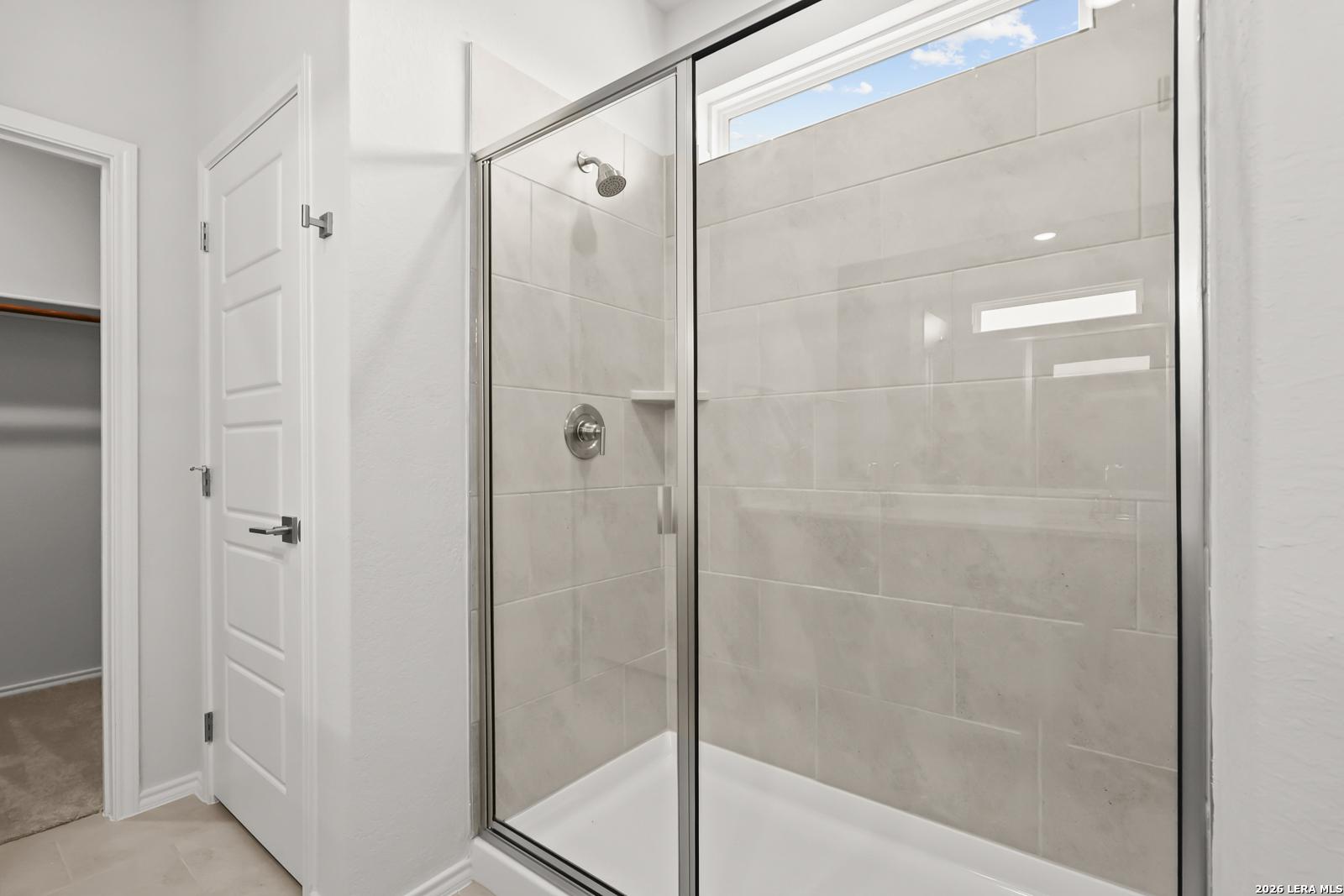 Glass-enclosed tile shower with transom window in master bathroom of Davidson Homes The Daphne I in Bricewood, San Antonio