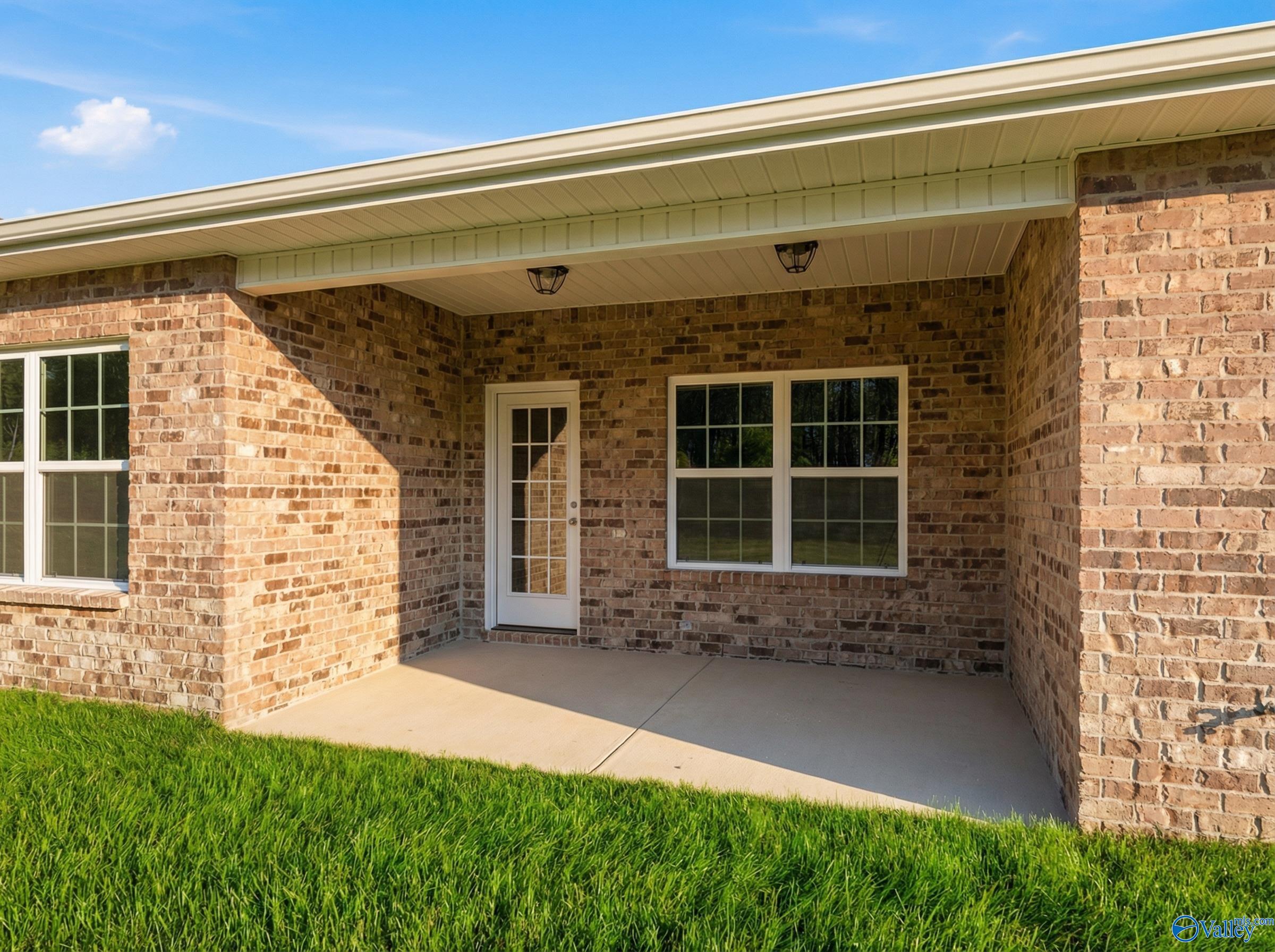 Brick home exterior with covered patio, glass door, windows, and lush green lawn in The Montgomery floor plan, Hartselle, Alabama