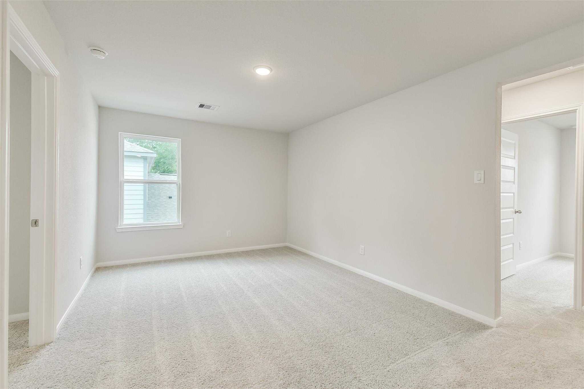 Spacious empty bedroom with neutral walls, beige carpet, large window, and doorways in Davidson Homes The Brazos F, Conroe, Texas
