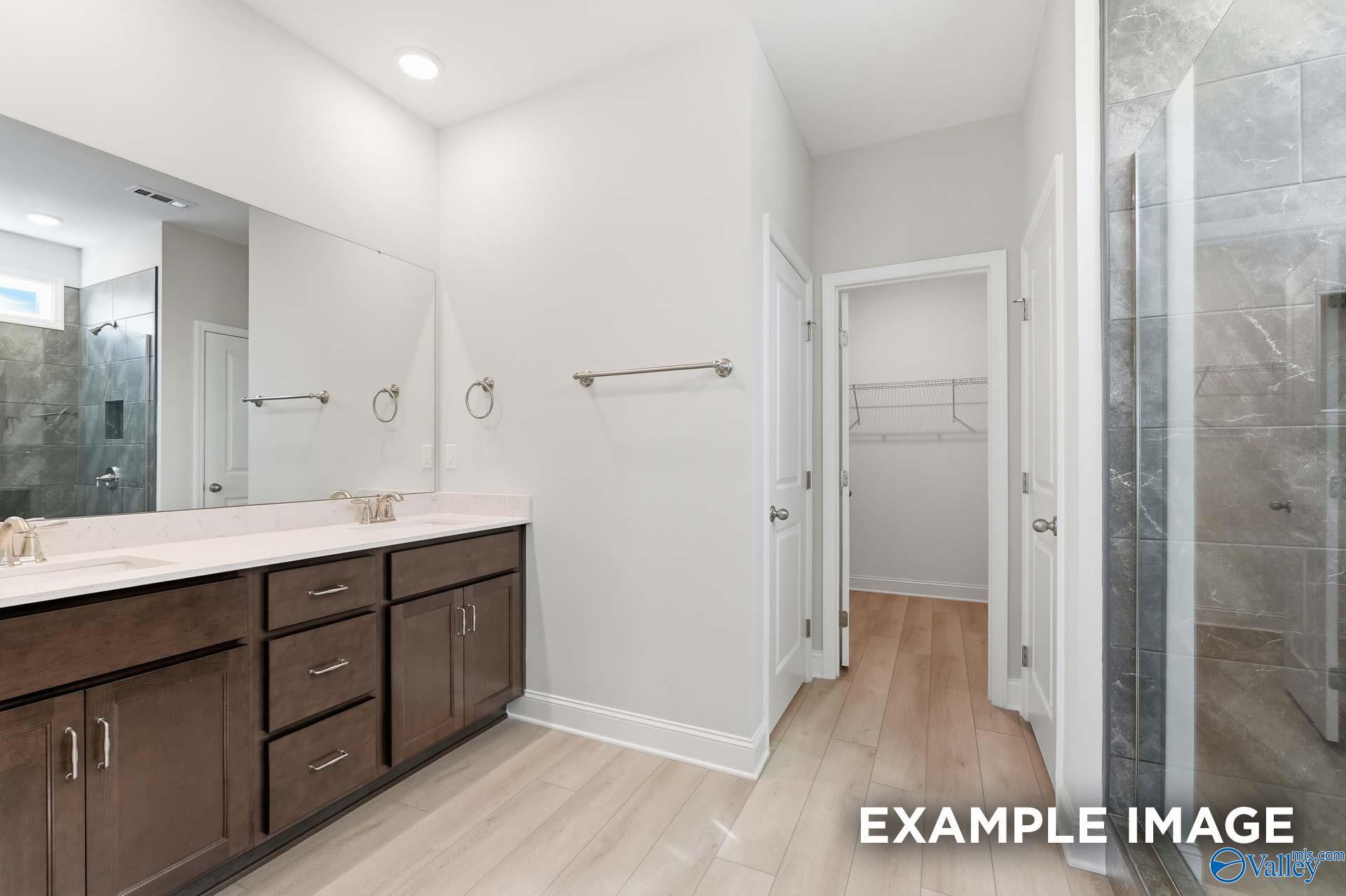Modern master bathroom with double quartz vanity, dark cabinets, frameless glass shower, and walk-in closet in Davidson Homes Harrison C, Madison AL