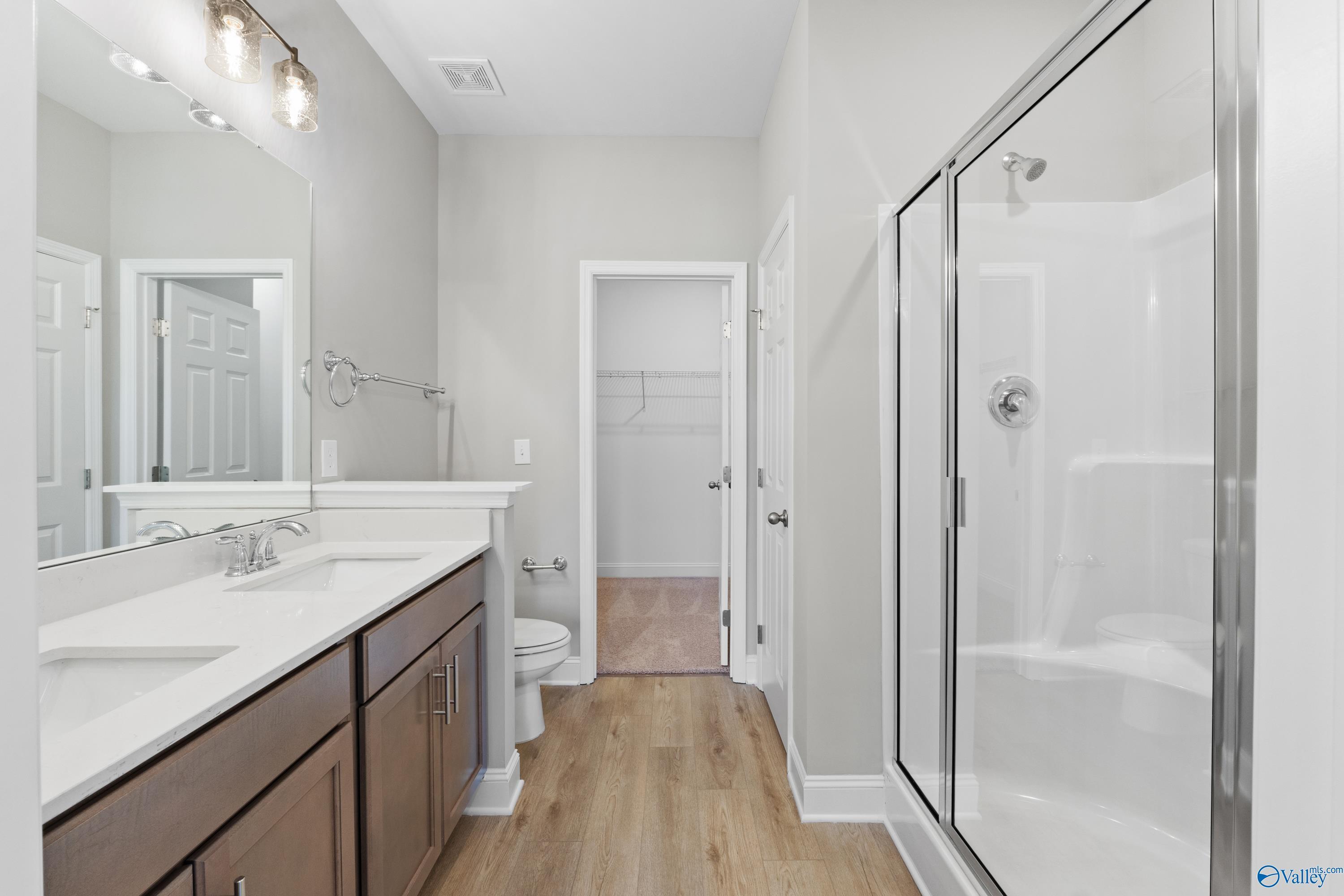 Modern master bathroom featuring double vanity, frameless glass shower, and walk-in closet in Davidson Homes The Asheville C, Athens AL
