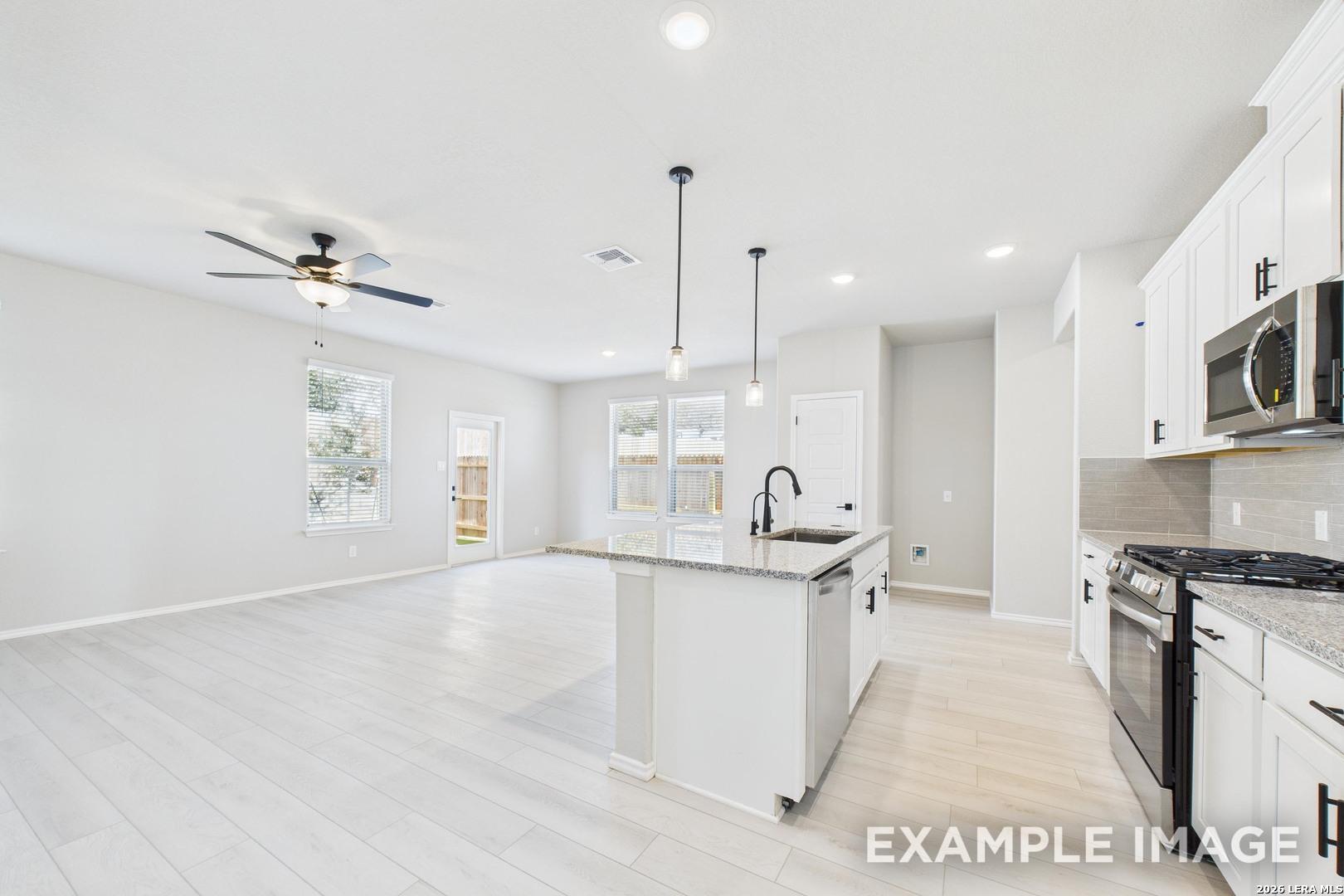 Open-concept kitchen and living area with white cabinets and granite island in The Charlotte B home in Cedar Heights, TX.