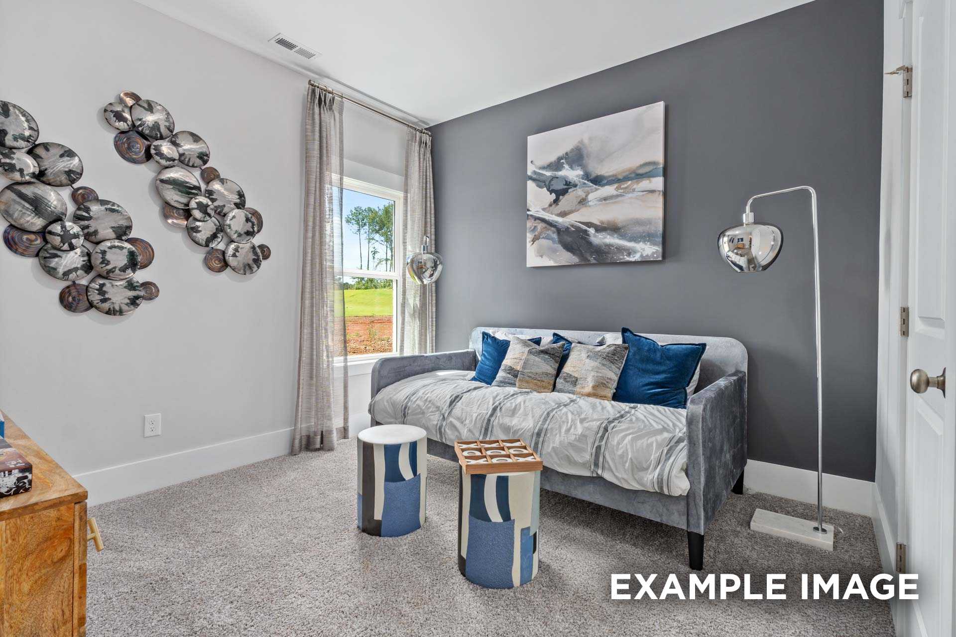Cozy gray bedroom in The Franklin C by Davidson Homes featuring tufted daybed with blue pillows, abstract wall art, and window to green field