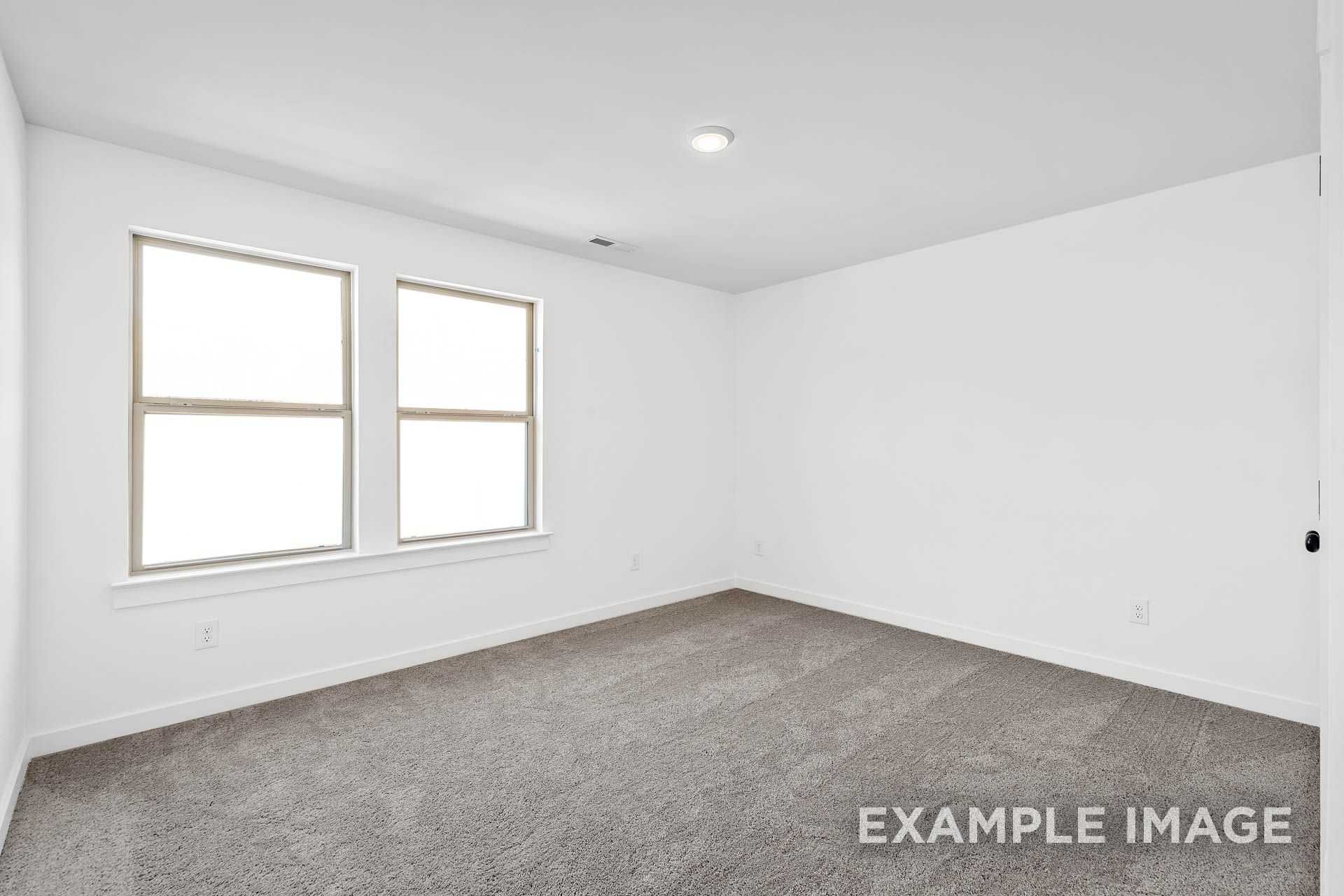 Spacious empty bedroom in The Logan B with white walls, large windows, and gray carpet flooring