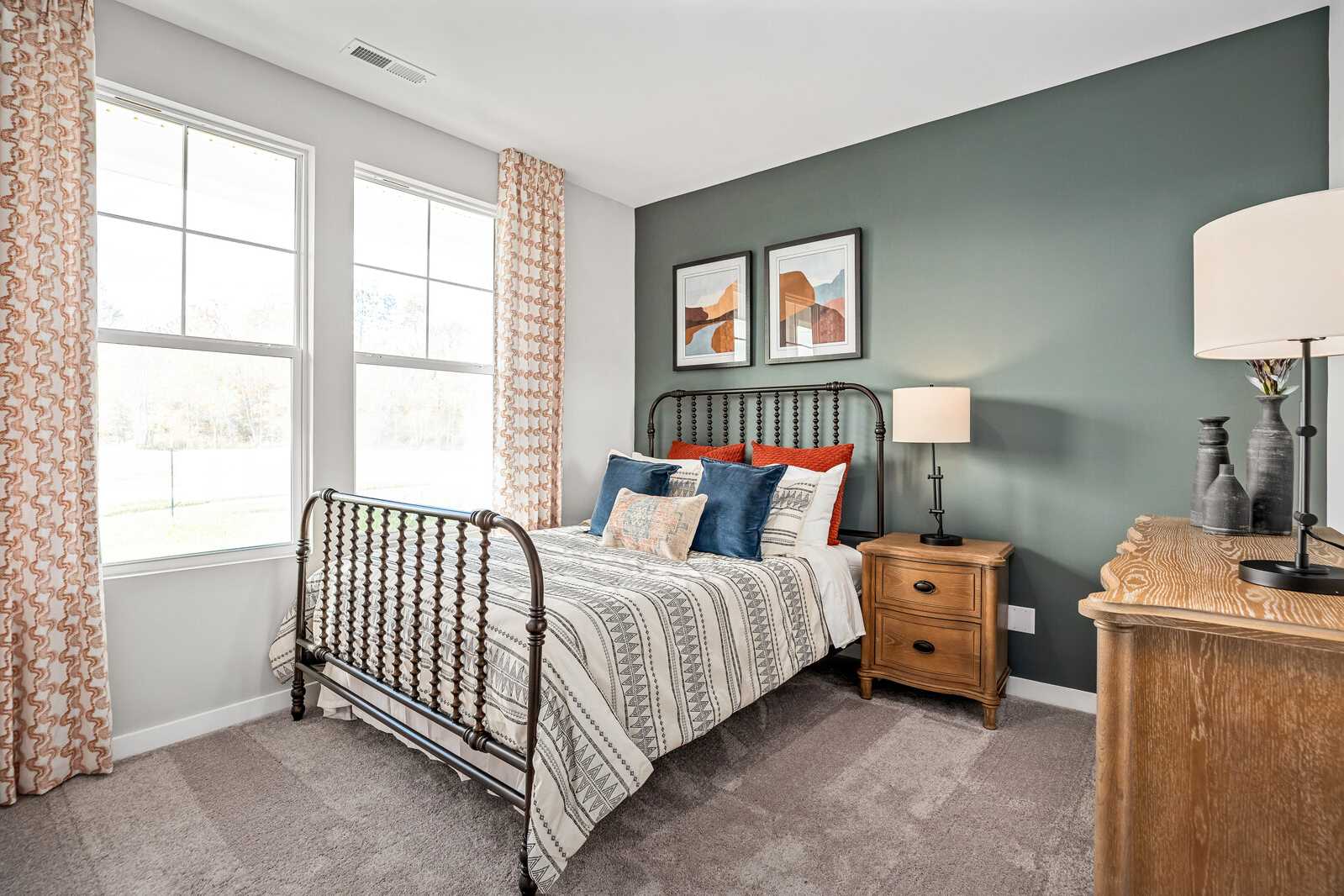 Cozy bedroom with wrought iron bed, colorful pillows, sage green walls, and orange curtains in Sage Farms, White House TN