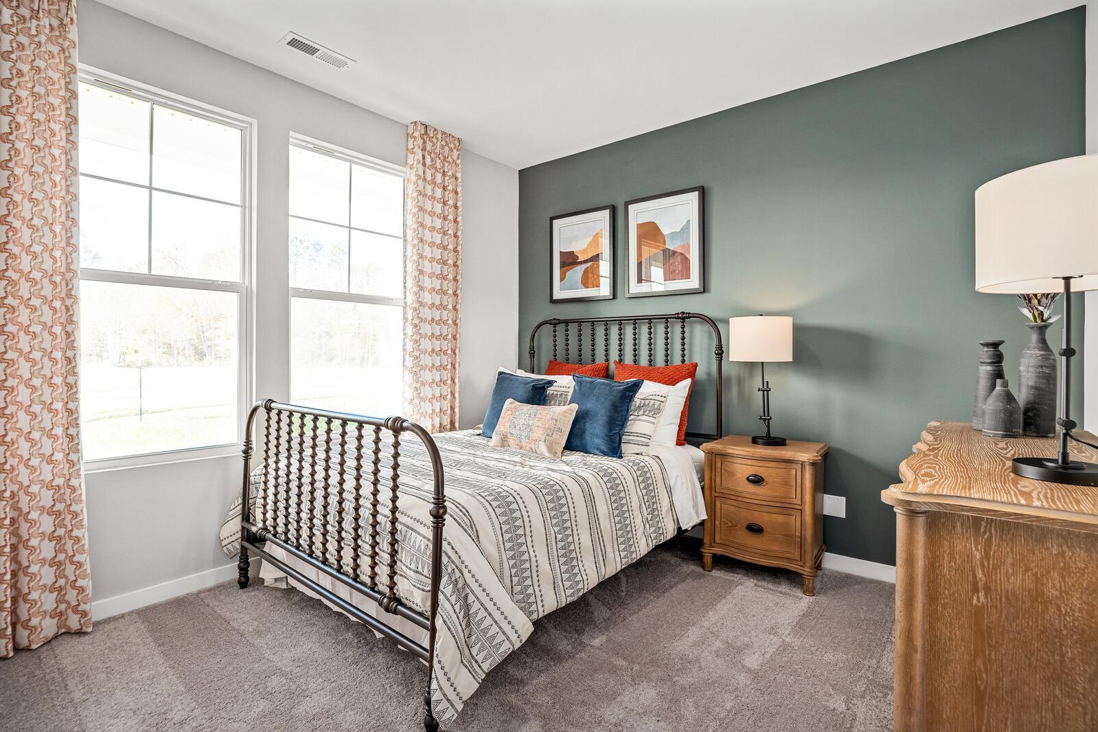Cozy bedroom with wrought iron bed, colorful pillows, sage green walls, and orange curtains in Sage Farms, White House TN