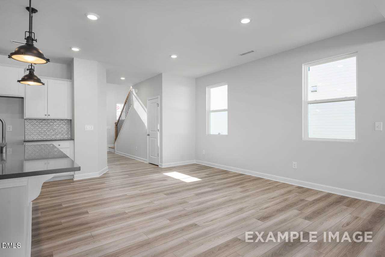 Open kitchen with white cabinets, stainless appliances, hardwood floors, and adjacent living space in The Adalynn A, Lillington, NC