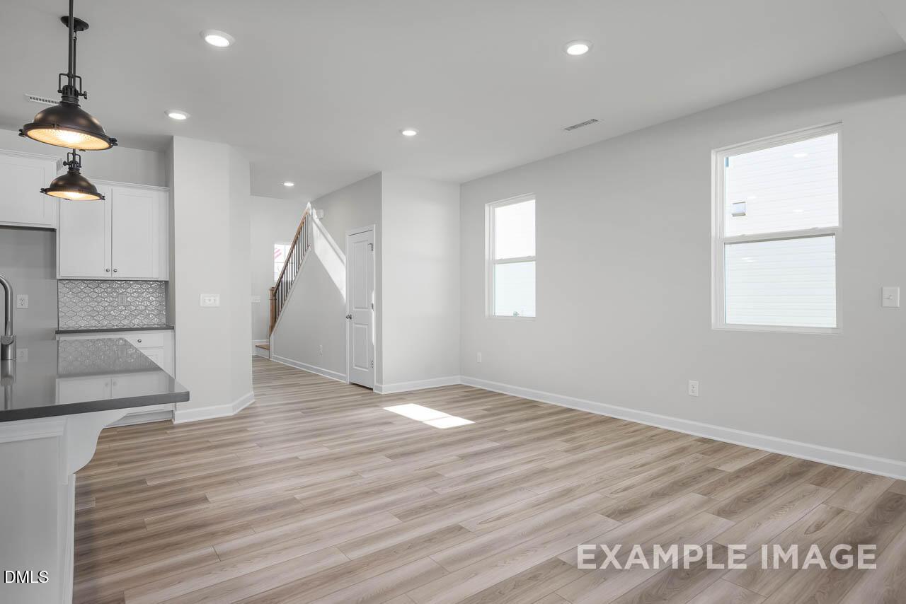 Open-concept kitchen with white cabinets, stainless sink, hardwood floors, and staircase in Davidson Homes Adalynn A, Lillington, NC