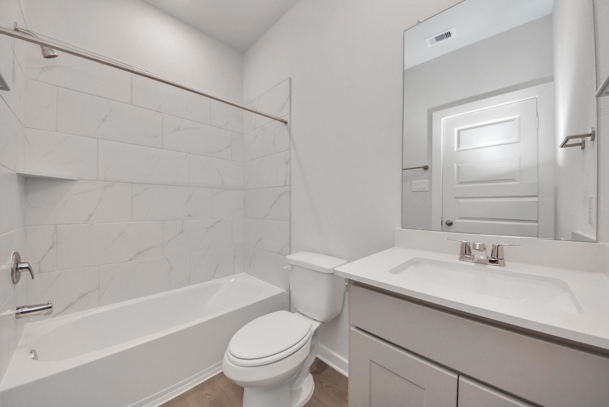 Modern bathroom with marble-tile tub, vanity sink, and toilet in Davidson Homes The San Marcos E, Beasley, Texas