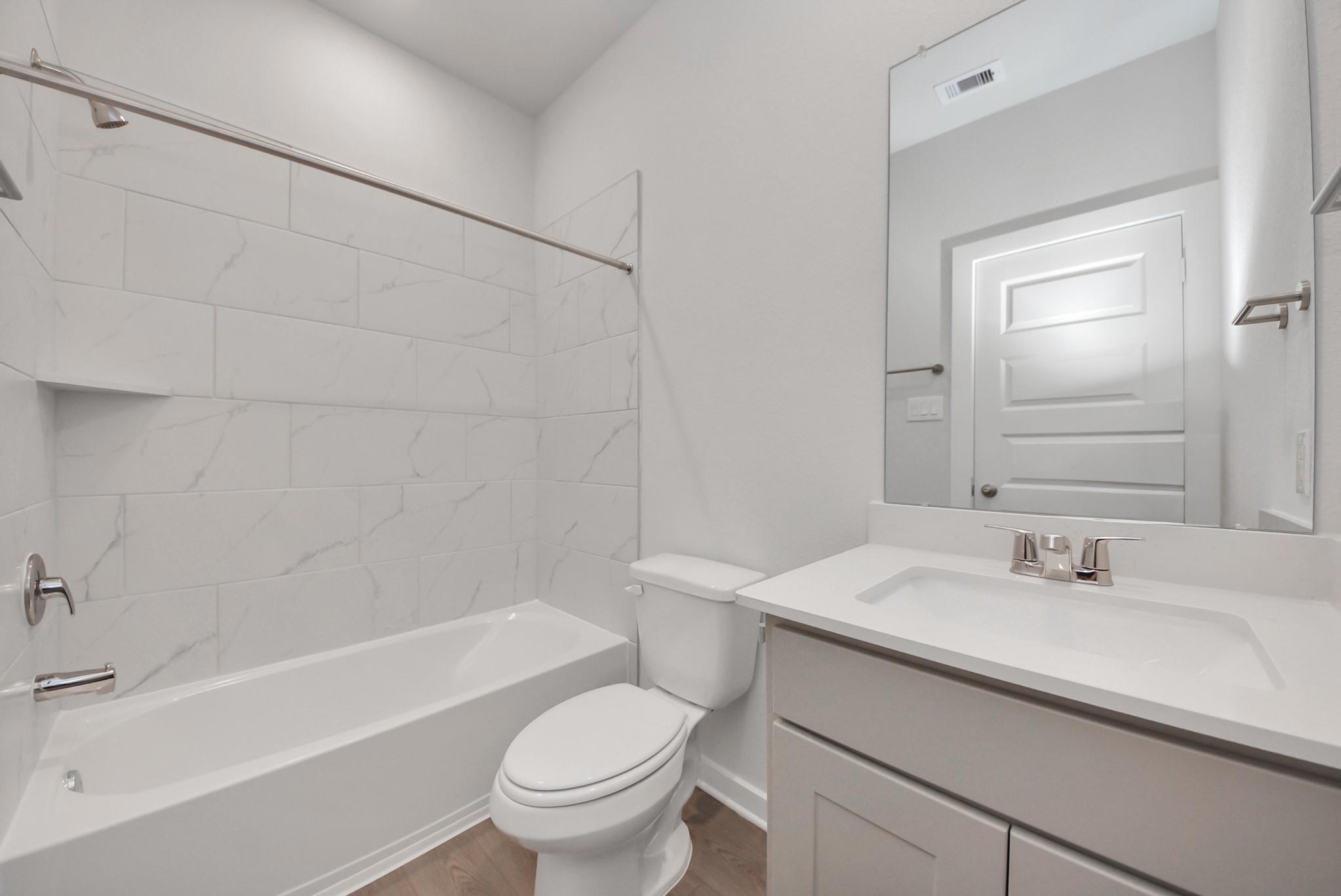 Modern bathroom with marble-tile tub, vanity sink, and toilet in Davidson Homes The San Marcos E, Beasley, Texas