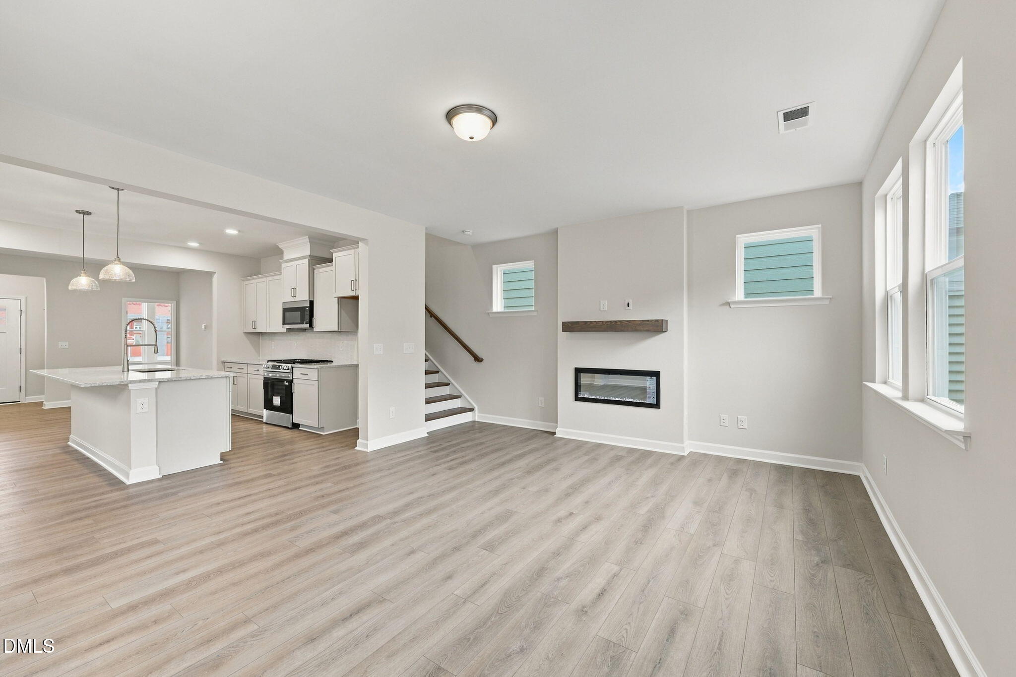 Open-concept living room and kitchen with white cabinetry, electric fireplace, and hardwood floors in Davidson Homes The Alexander B, Knightdale