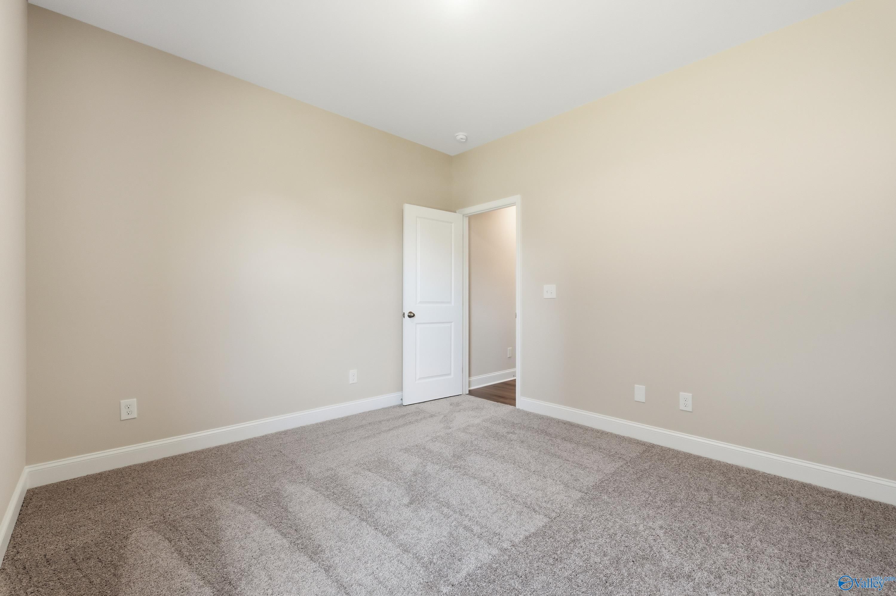 Empty bedroom with beige walls, plush gray carpet, and white interior door in Davidson Homes The Everett, Creekside, Harvest, Alabama
