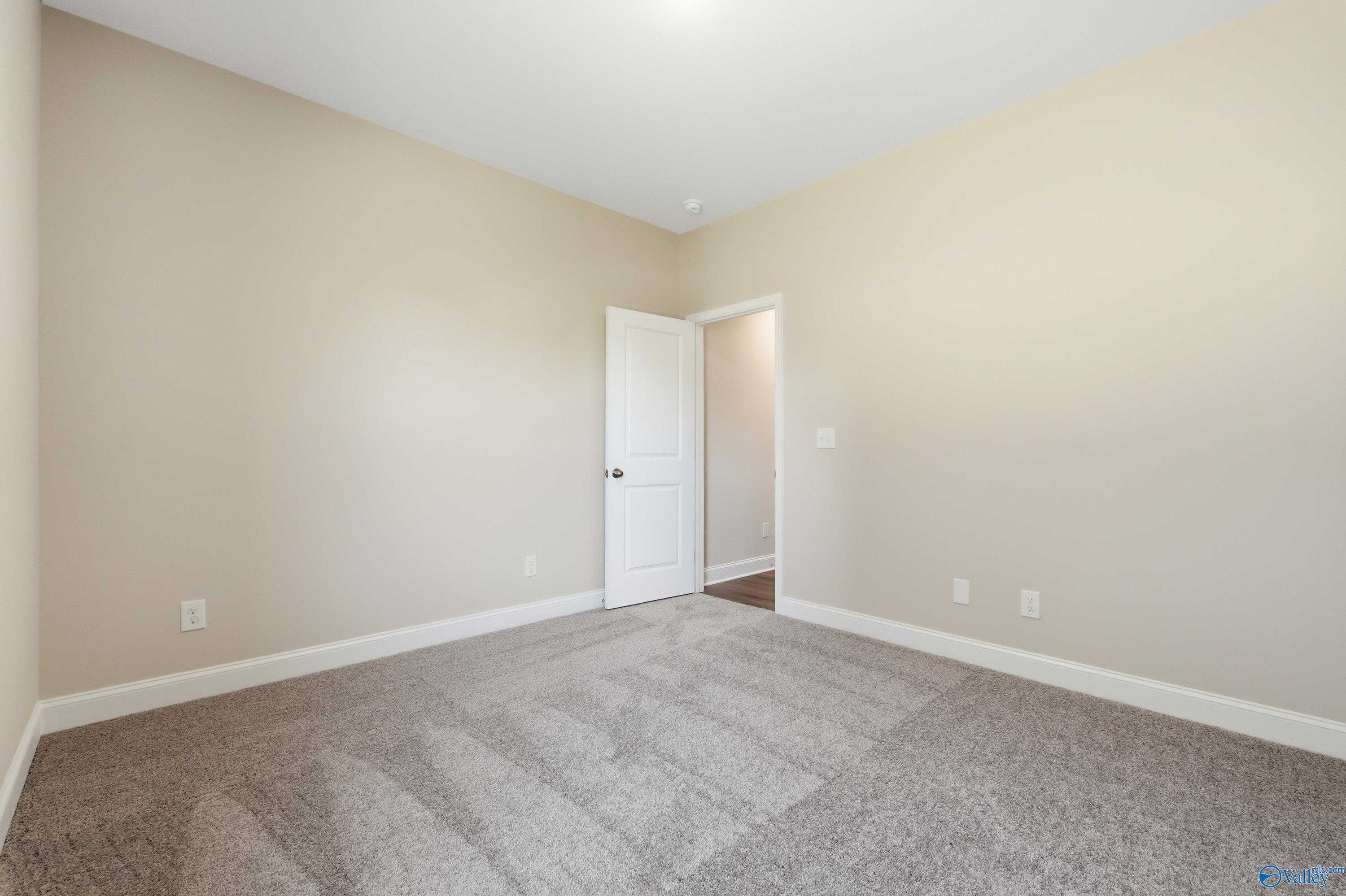 Empty bedroom with beige walls, plush gray carpet, and white interior door in Davidson Homes The Everett, Creekside, Harvest, Alabama