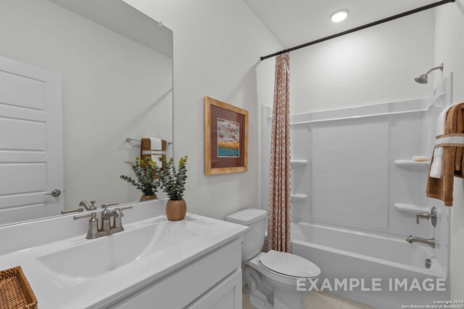Modern white bathroom with deep tub, patterned shower curtain, large mirror, and vanity in Davidson Homes The Daphne K, San Antonio