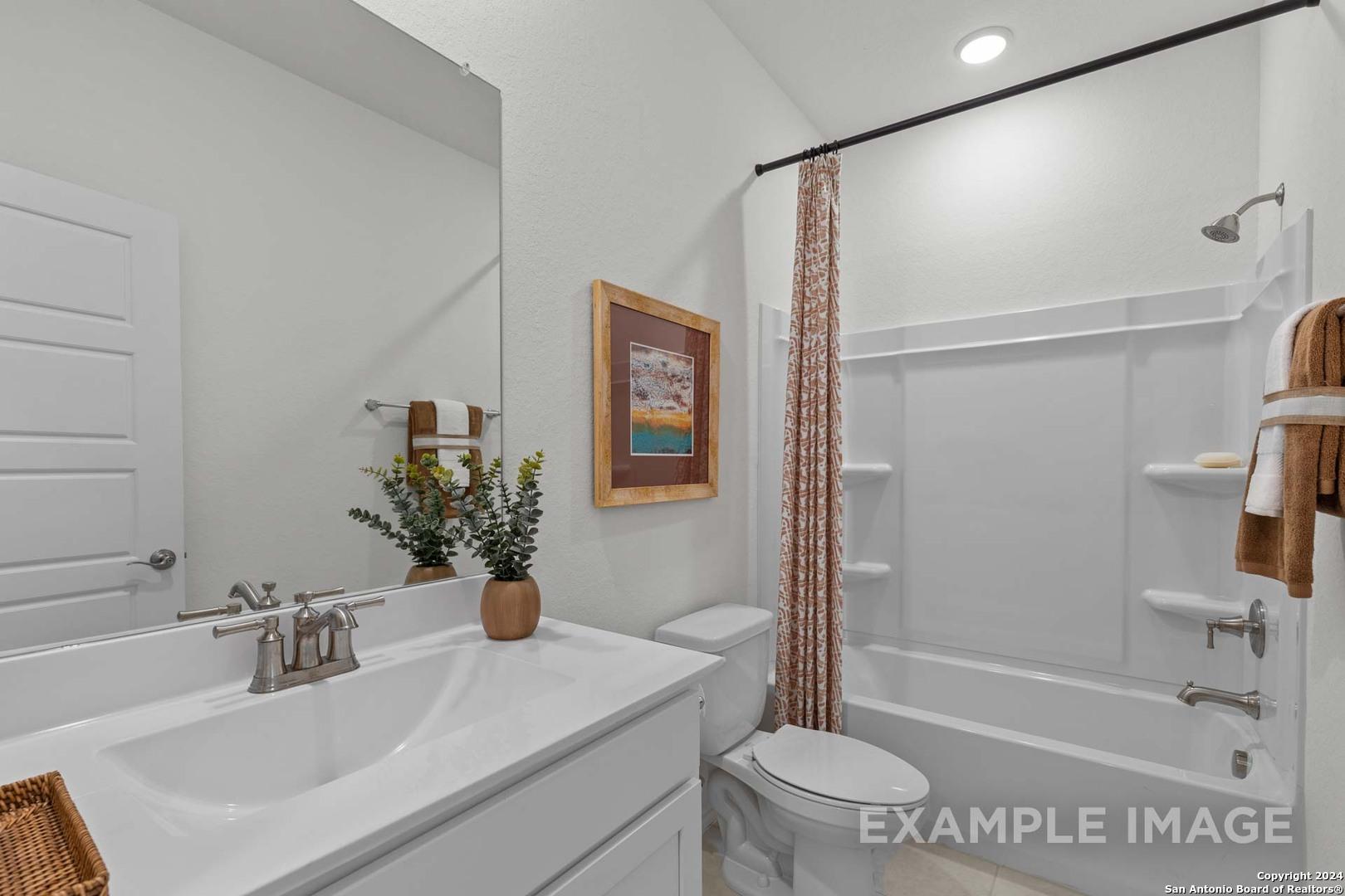 Modern white bathroom with deep tub, patterned shower curtain, large mirror, and vanity in Davidson Homes The Daphne K, San Antonio