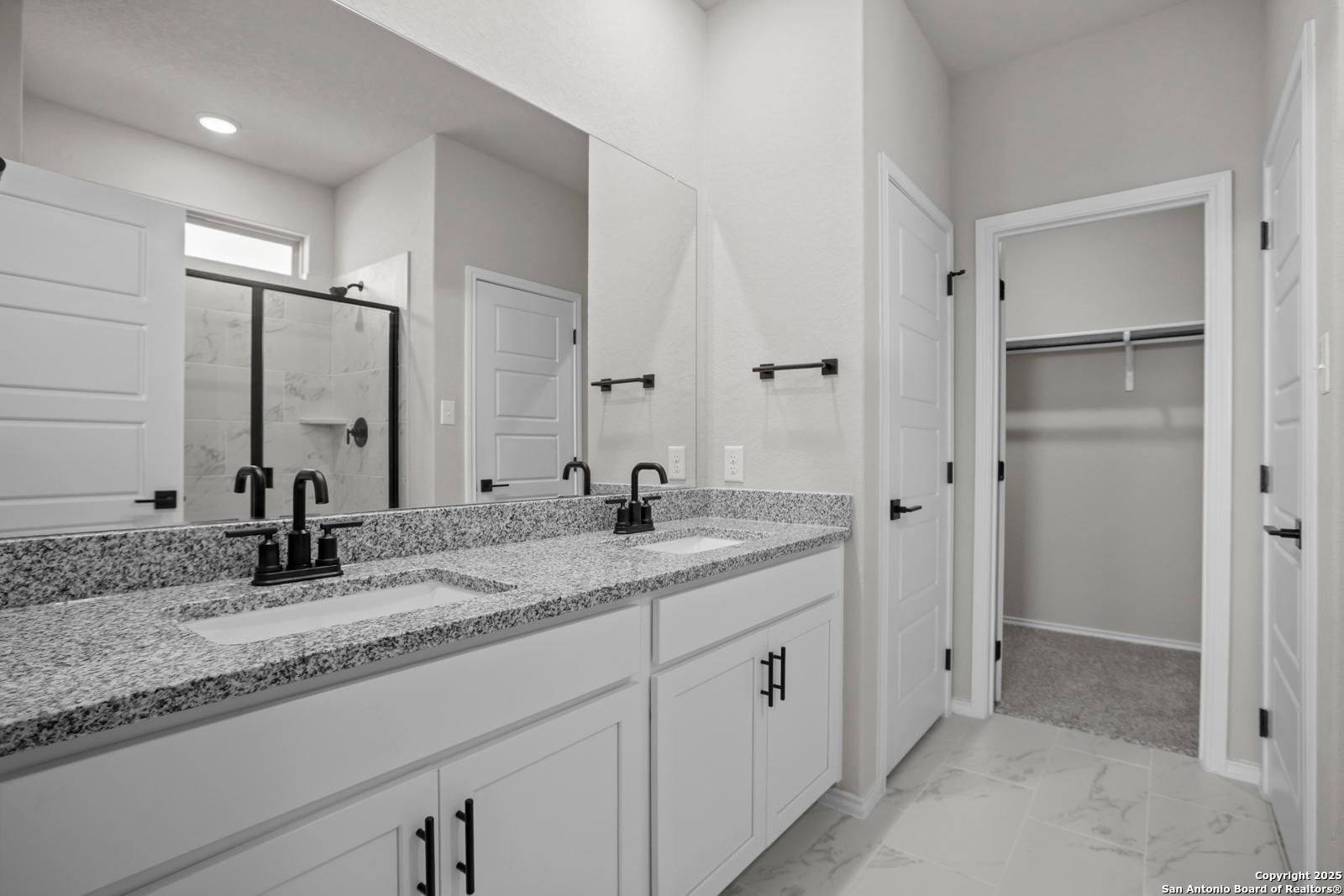 Elegant master bath with double granite vanity, glass shower, and walk-in closet in Davidson Homes The Daphne H, Seguin, TX