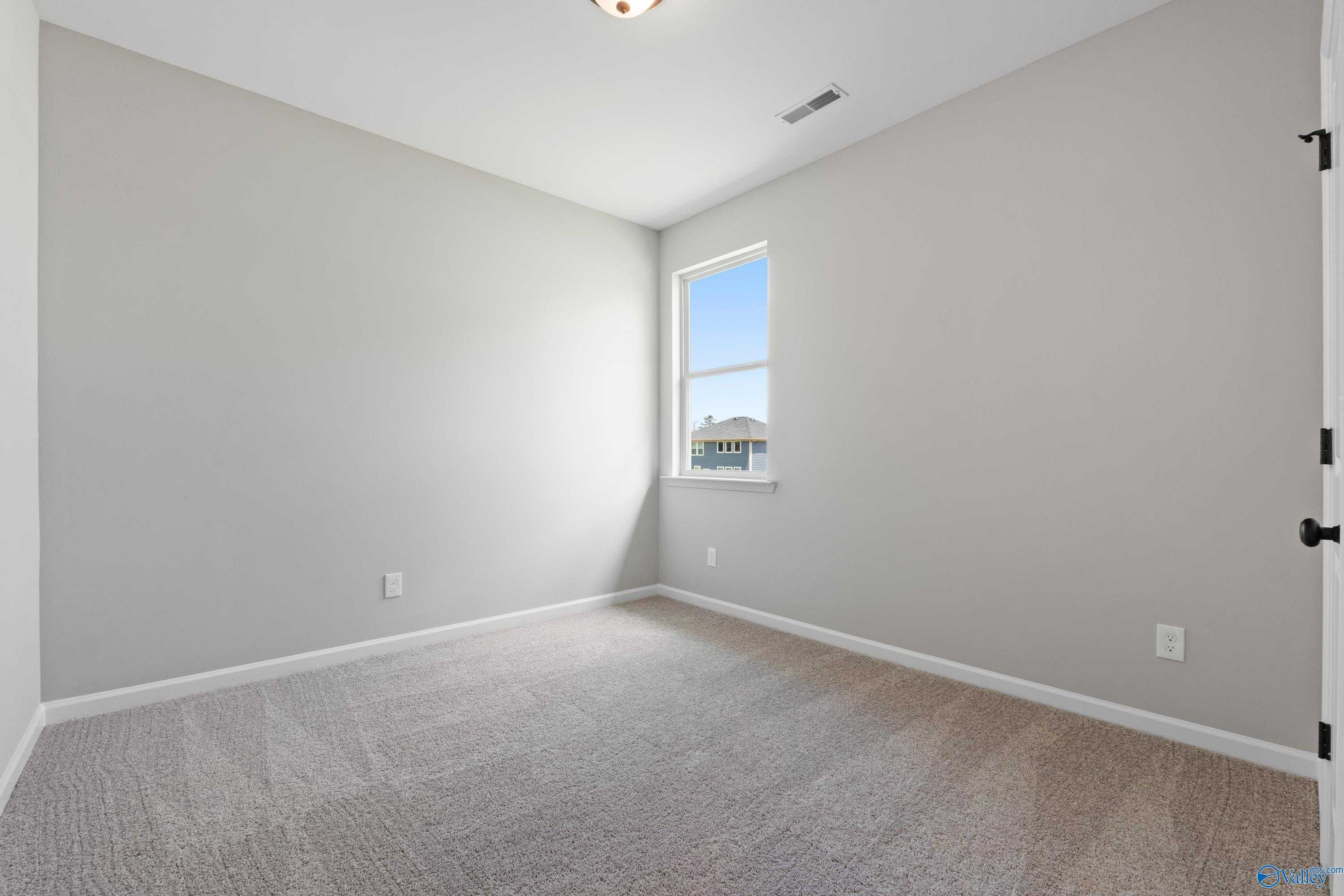 Bright empty bedroom featuring light gray walls, large window with natural light, and beige carpet in The Nantucket home, Madison, Alabama