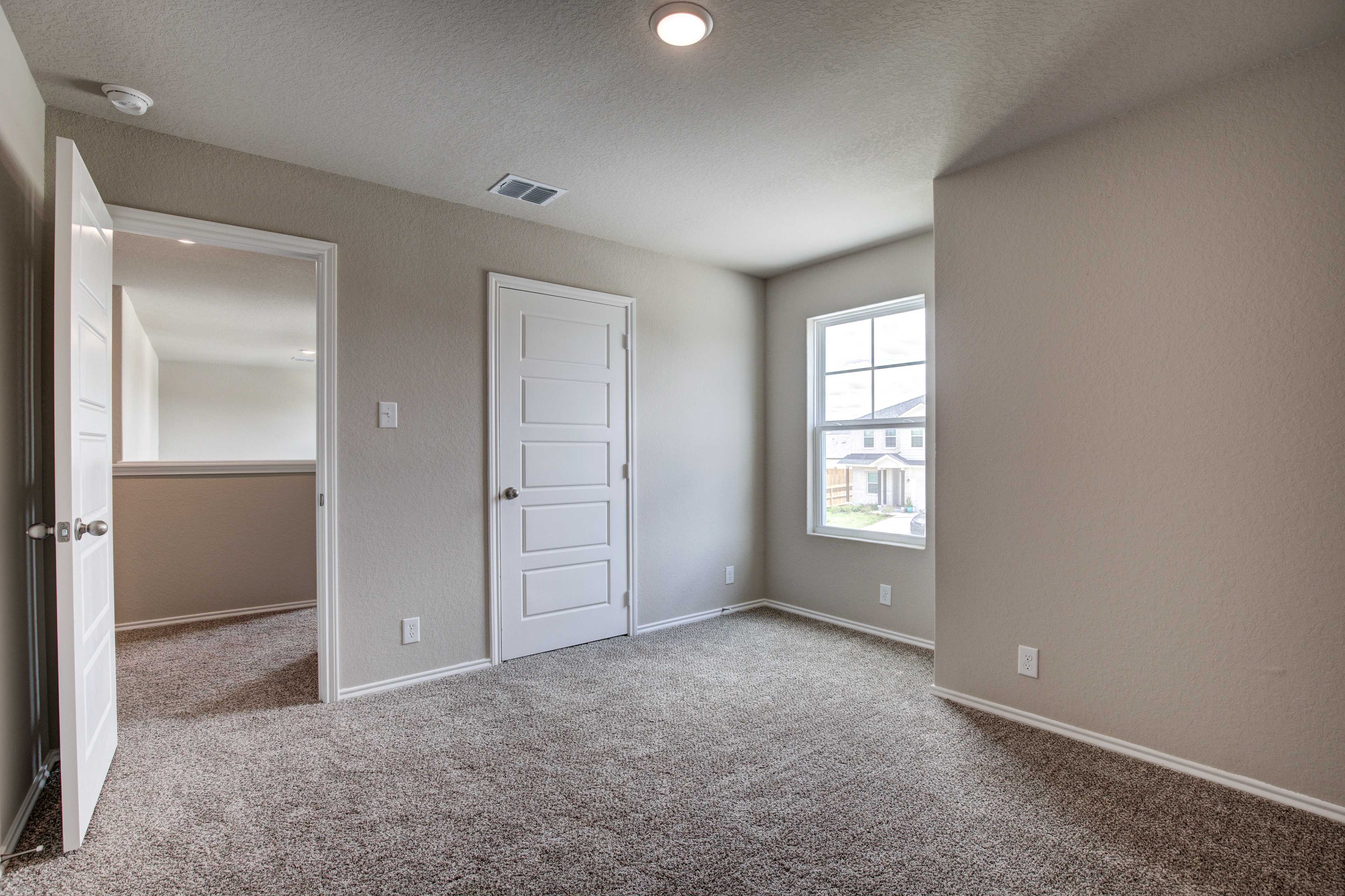 Spacious empty master bedroom in The Murray Davidson Homes design with beige walls, carpeted floor, large window, and ensuite door