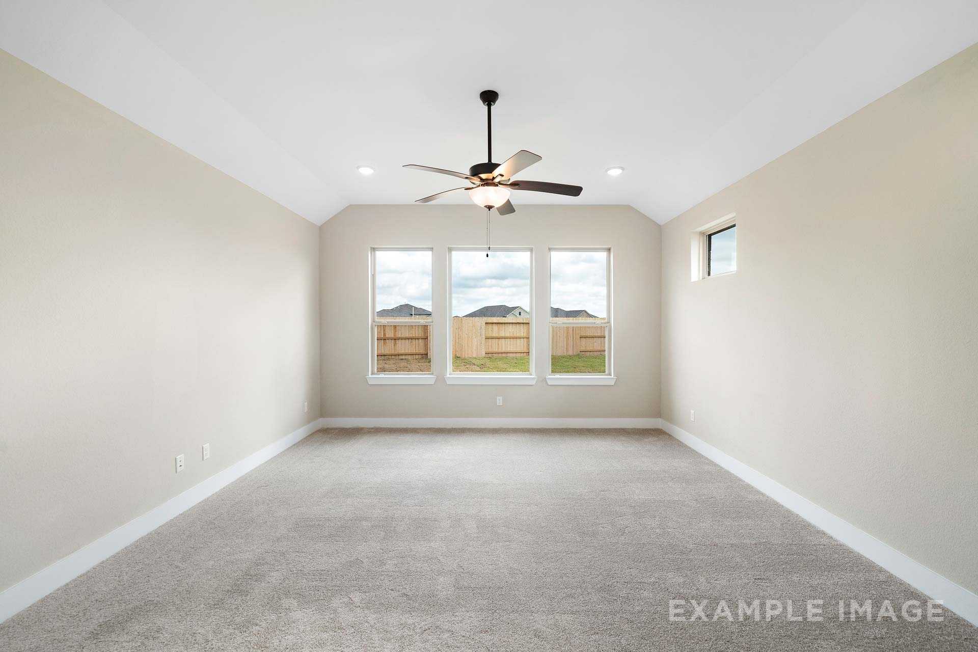 Spacious master bedroom in The Elizabeth A with neutral beige walls, ceiling fan, large triple windows, and carpeted floor