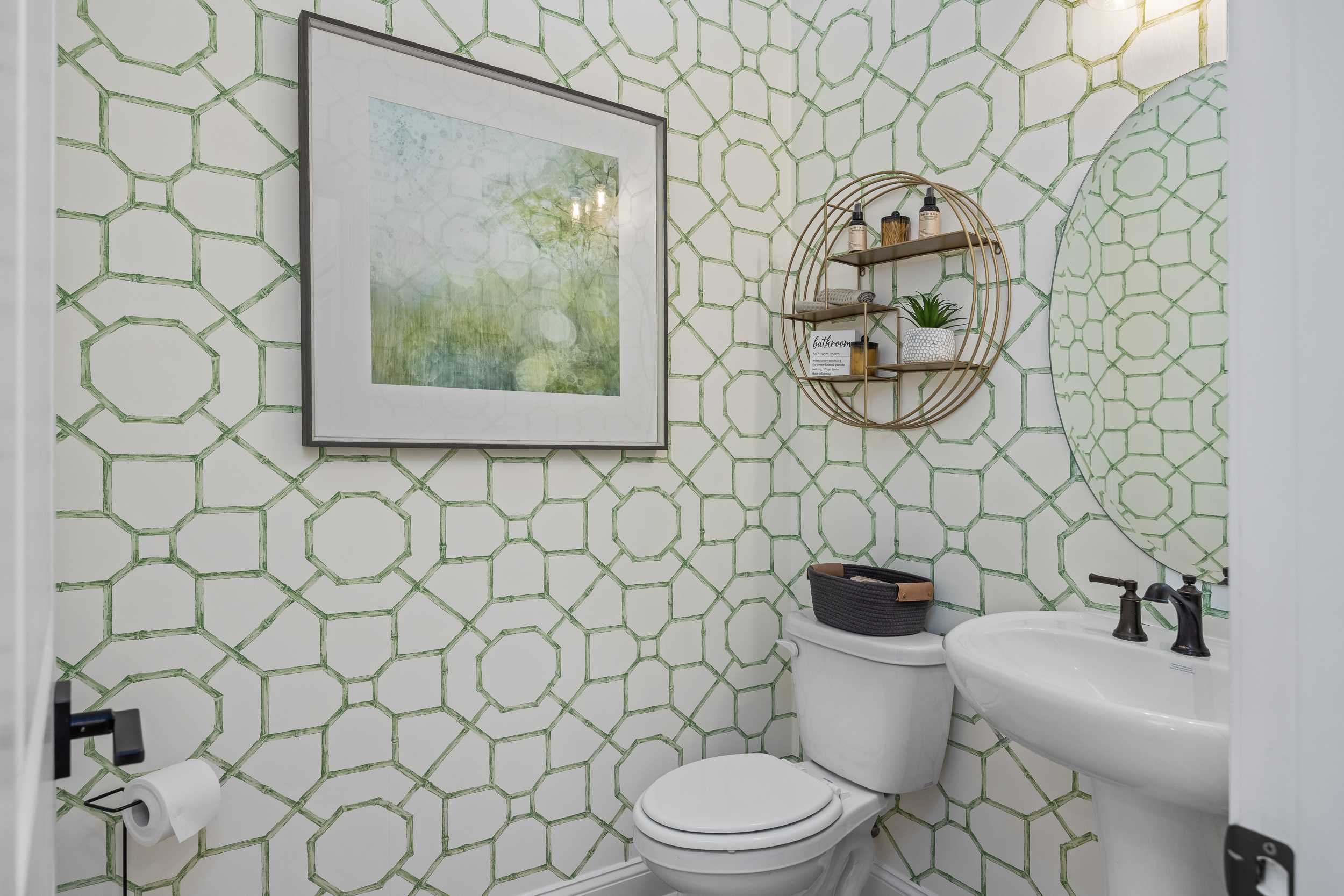 Elegant powder room at Laneridge Estates in Raleigh NC with geometric green wallpaper, pedestal sink, gold shelves, and round mirror