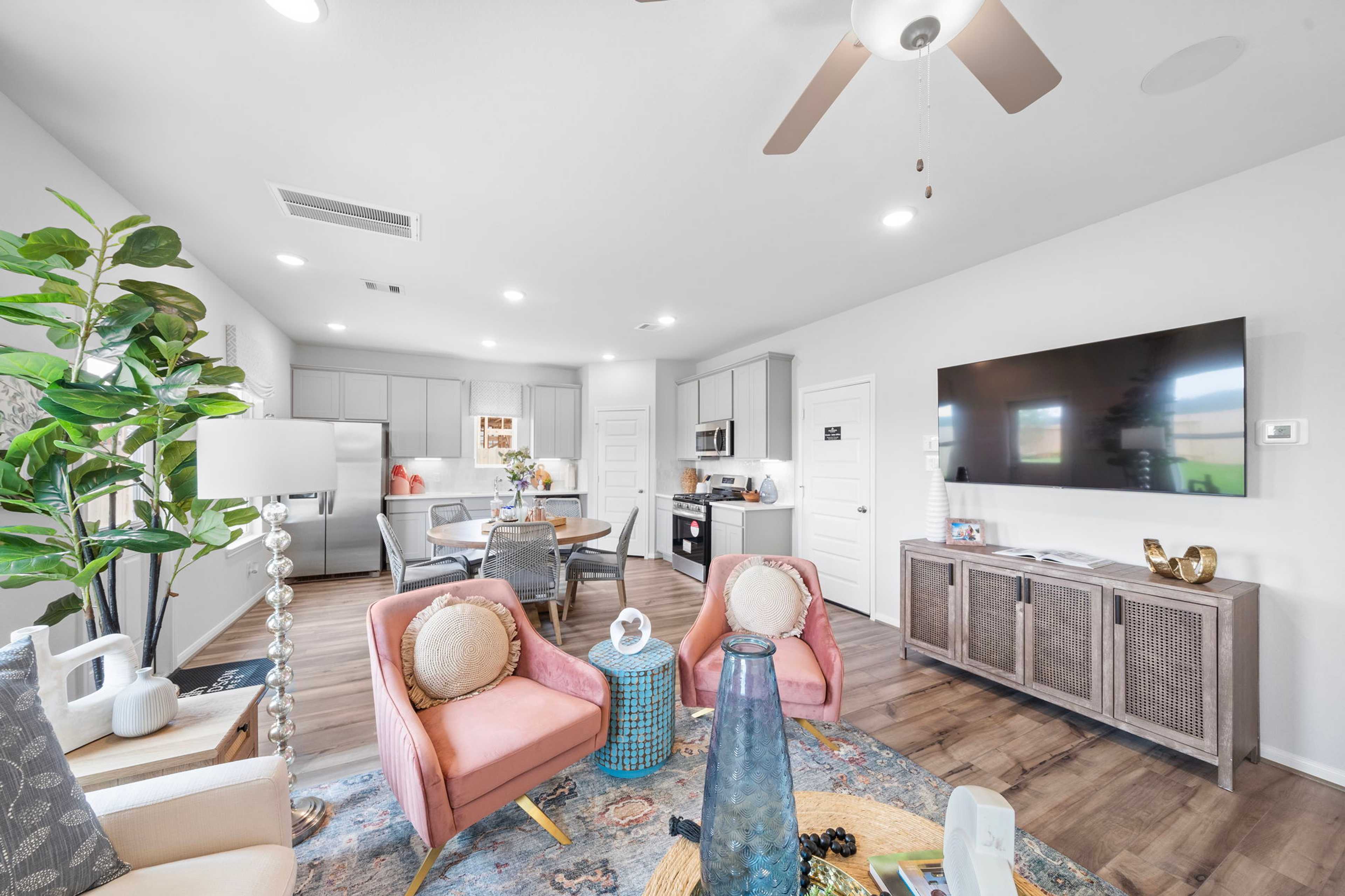 Open-concept living room and kitchen at Spring Branch Crossing in Conroe Texas featuring pink armchairs, hardwood floors, and white cabinetry