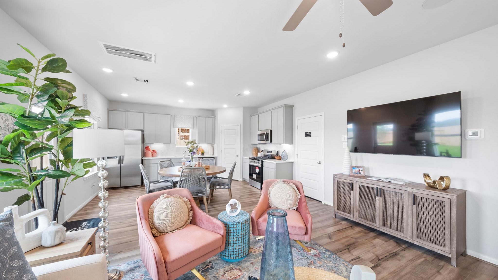 Open-concept living room and kitchen at Spring Branch Crossing in Conroe Texas featuring pink armchairs, hardwood floors, and white cabinetry