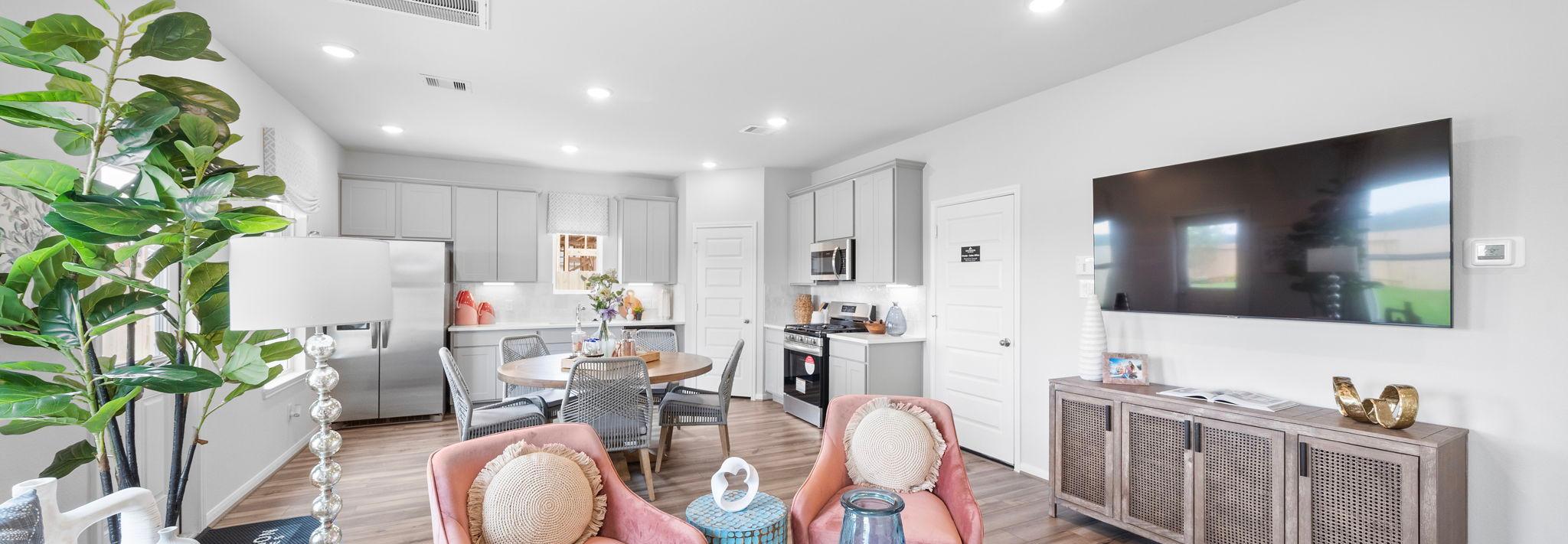 Open-concept living room and kitchen at Spring Branch Crossing in Conroe Texas featuring pink armchairs, hardwood floors, and white cabinetry