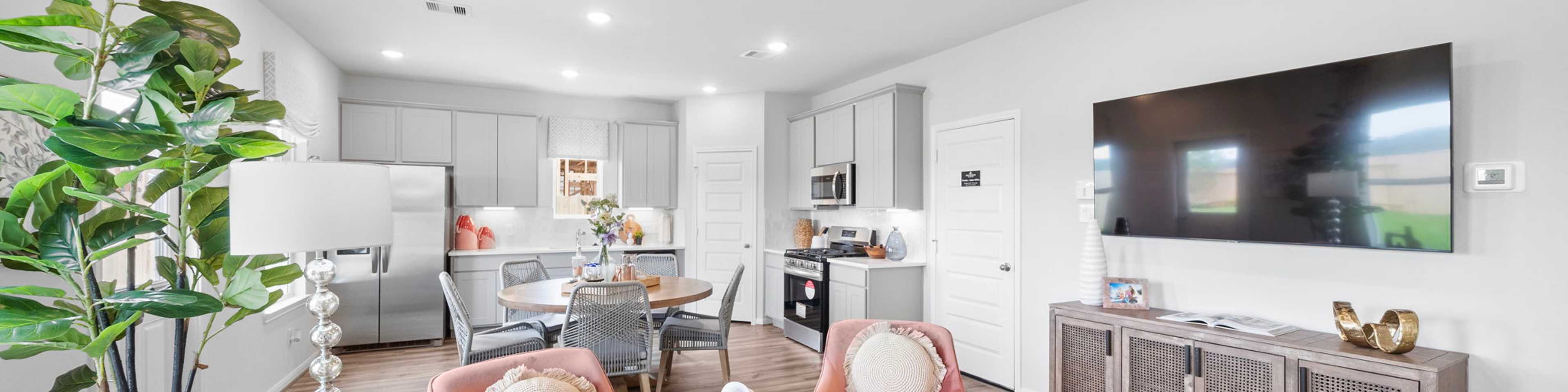 Open-concept living room and kitchen at Spring Branch Crossing in Conroe Texas featuring pink armchairs, hardwood floors, and white cabinetry
