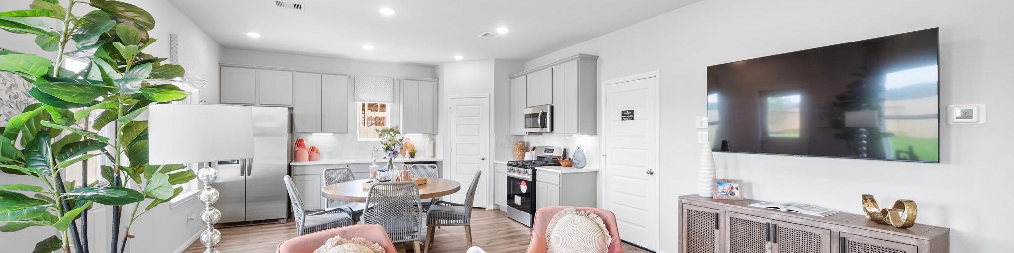 Open-concept living room and kitchen at Spring Branch Crossing in Conroe Texas featuring pink armchairs, hardwood floors, and white cabinetry
