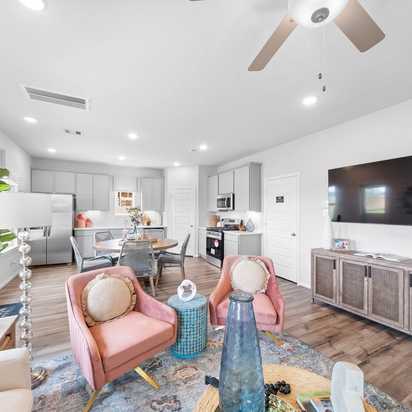 Open-concept living room and kitchen at Spring Branch Crossing in Conroe Texas featuring pink armchairs, hardwood floors, and white cabinetry