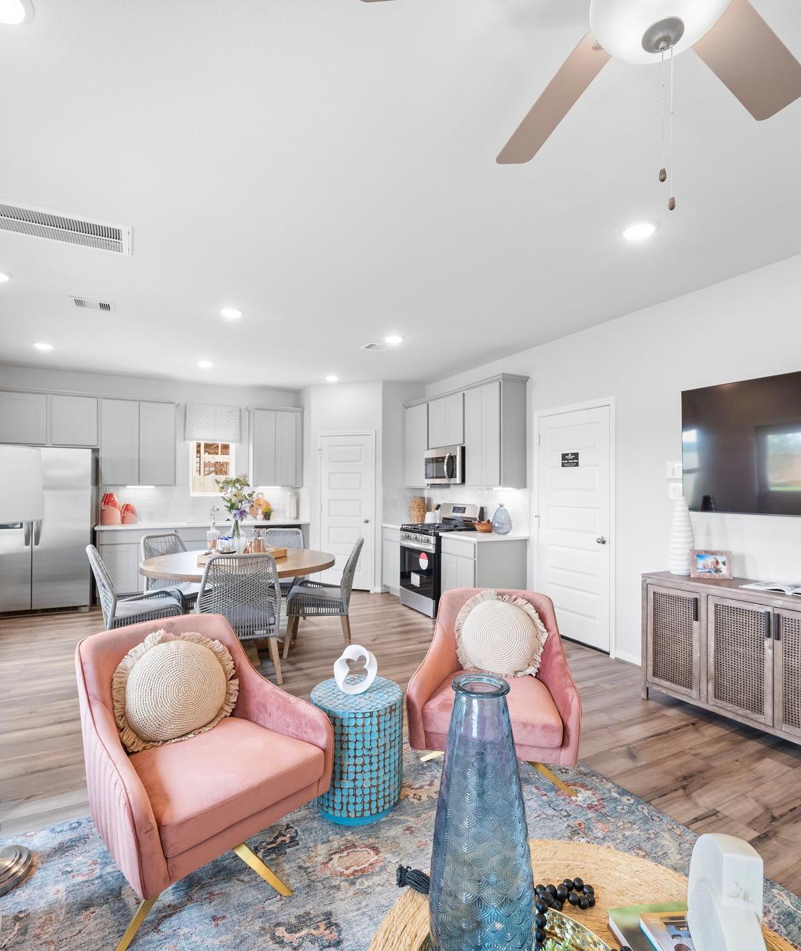 Open-concept living room and kitchen at Spring Branch Crossing in Conroe Texas featuring pink armchairs, hardwood floors, and white cabinetry