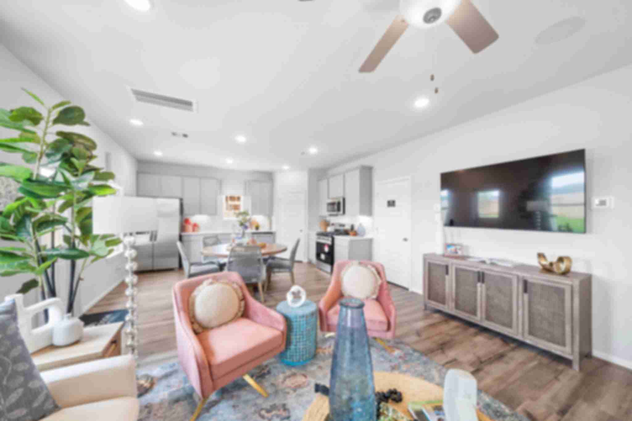 Open-concept living room and kitchen at Spring Branch Crossing in Conroe Texas featuring pink armchairs, hardwood floors, and white cabinetry