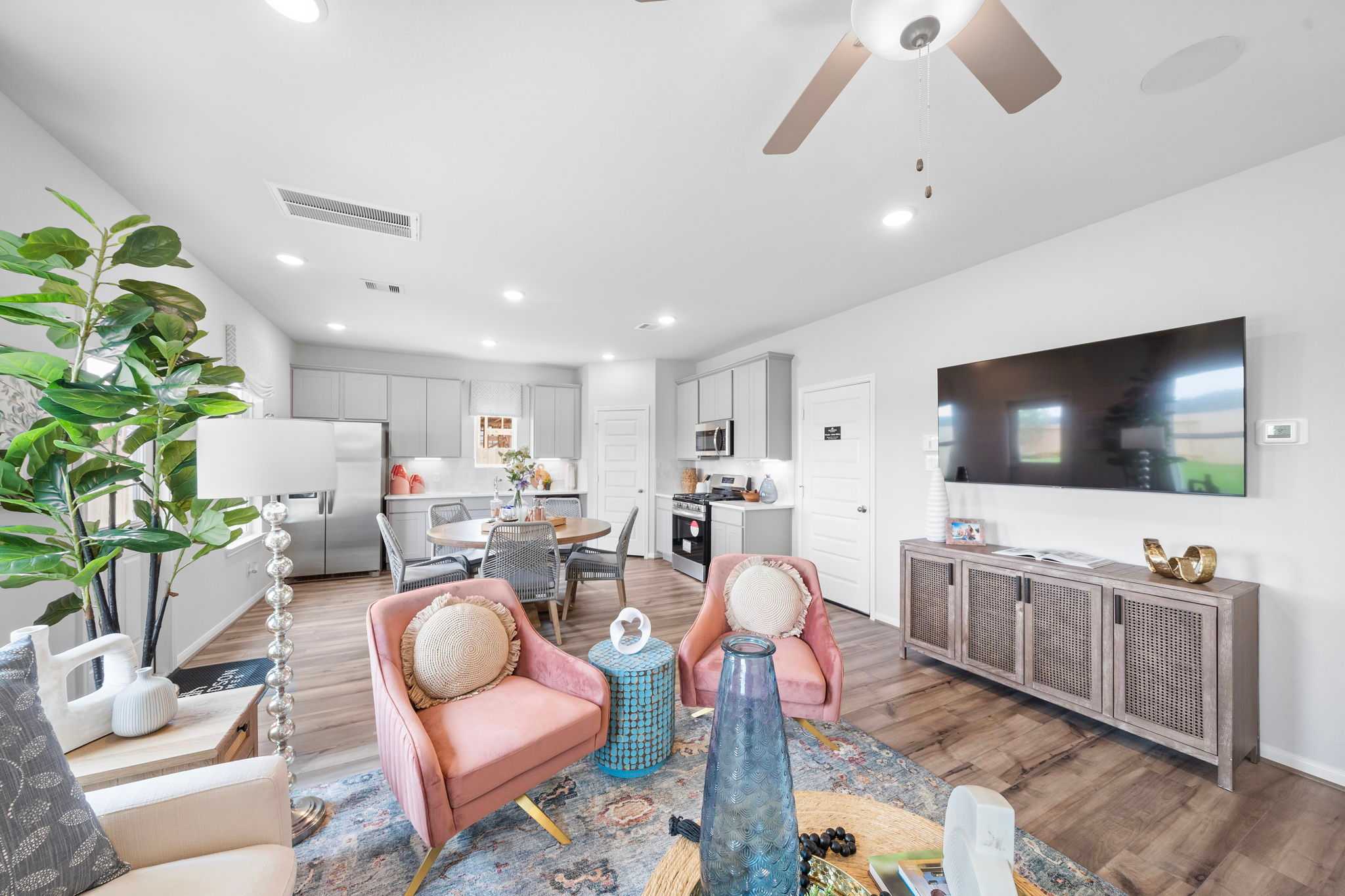 Spacious open-concept living room and kitchen at Spring Branch Crossing in Conroe Texas with pink armchairs hardwood floors and potted plants